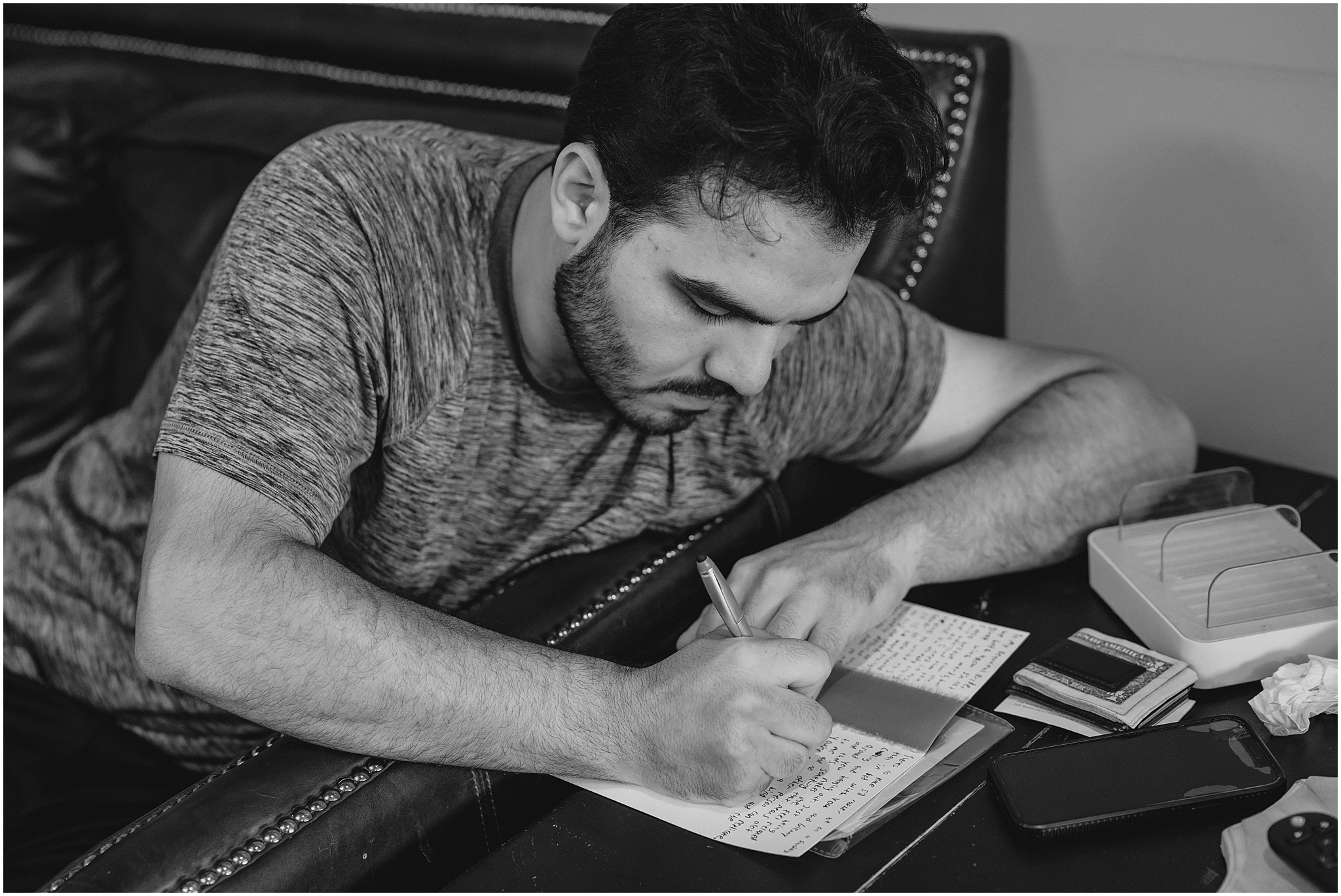 groom leans over leather couch to write letter to bride on wedding day in Andover NJ