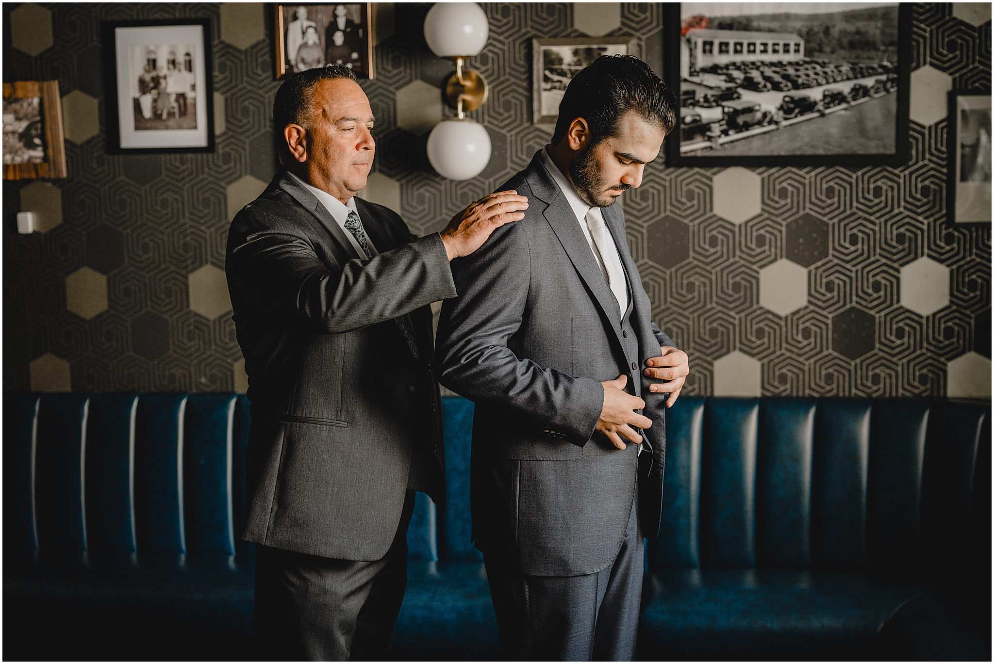 father helps groom into grey suit jacket in groom's suite at the Refinery at Perona Farms