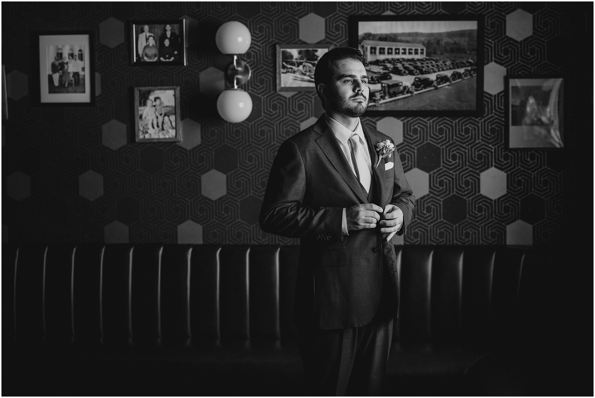 groom buttons up suit jacket standing in front of leather couch in groom's suite