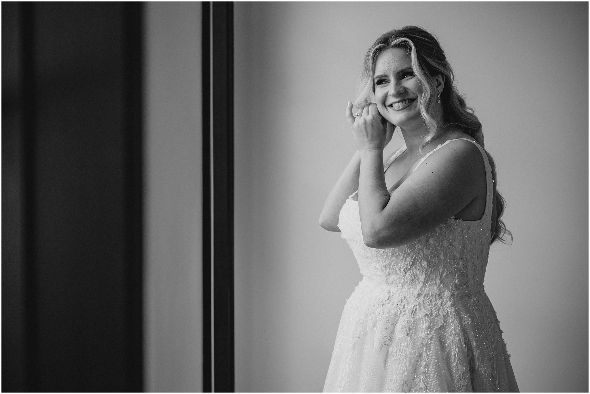 bride faces window adjusting earring in bridal suite at the Refinery at Perona Farms