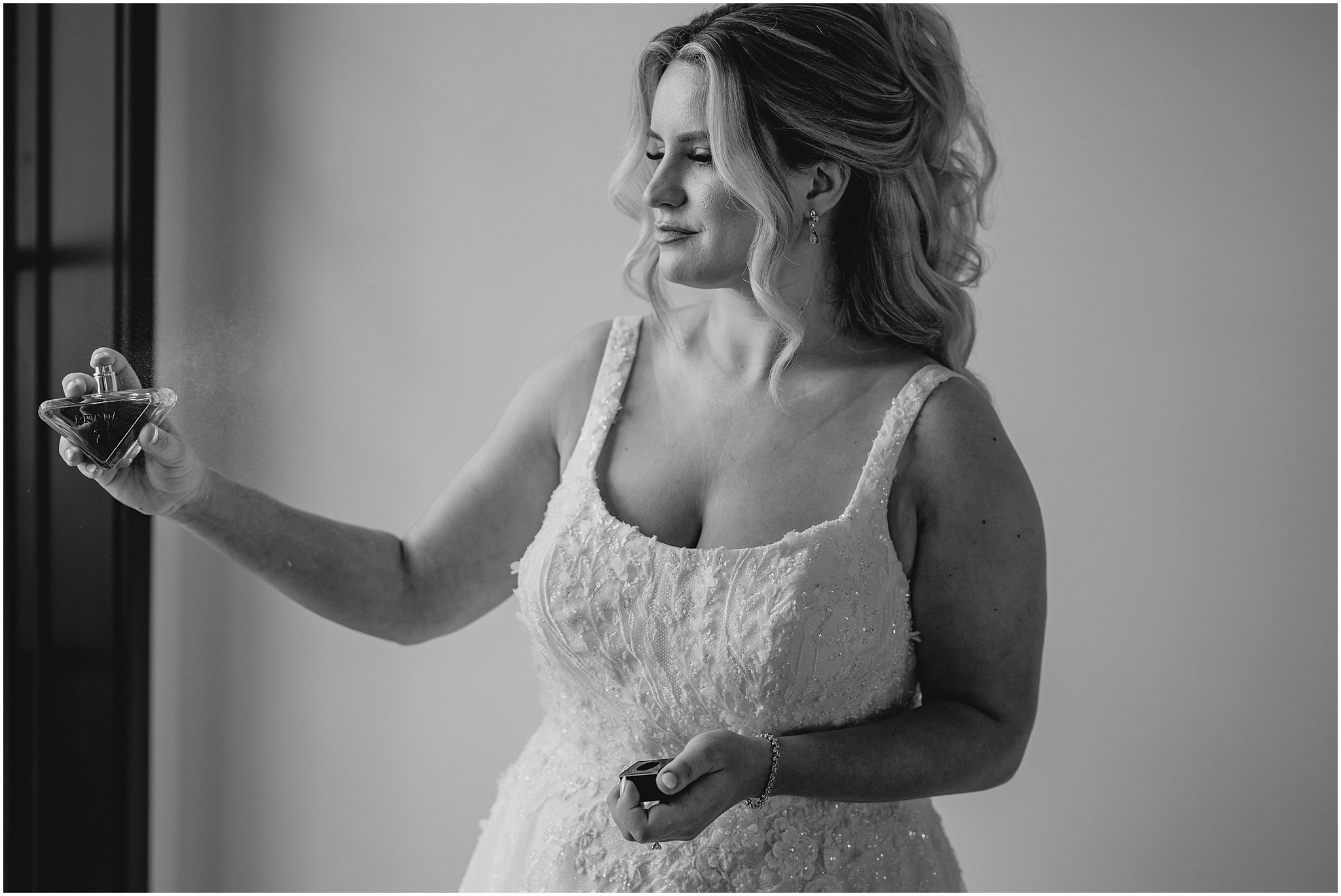 bride sprays perfume standing in front of mirror wearing wedding dress in suite at the Refinery at Perona Farms