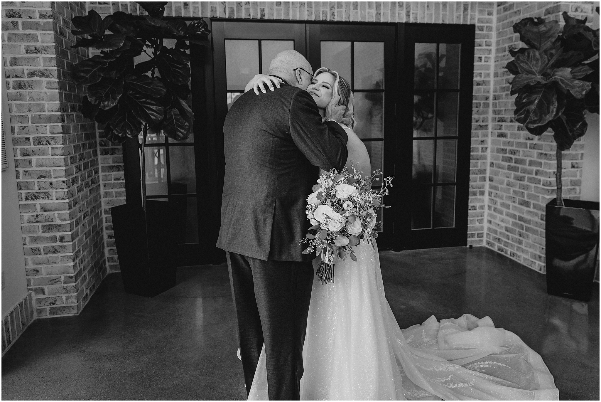 dad kisses bride's cheek hugging her in front of doors at the Refinery at Perona Farms
