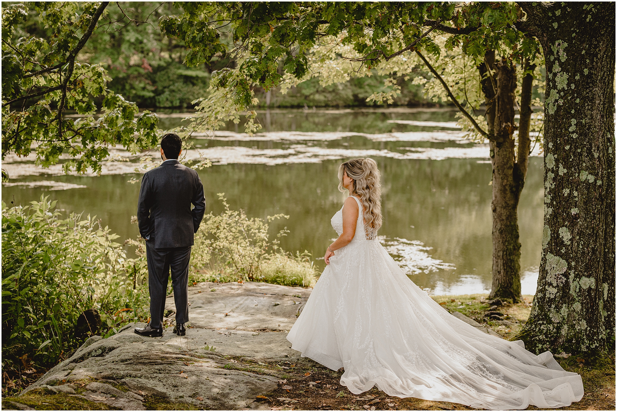 bride approaches groom for first look on rock by pond at the Refinery at Perona Farms