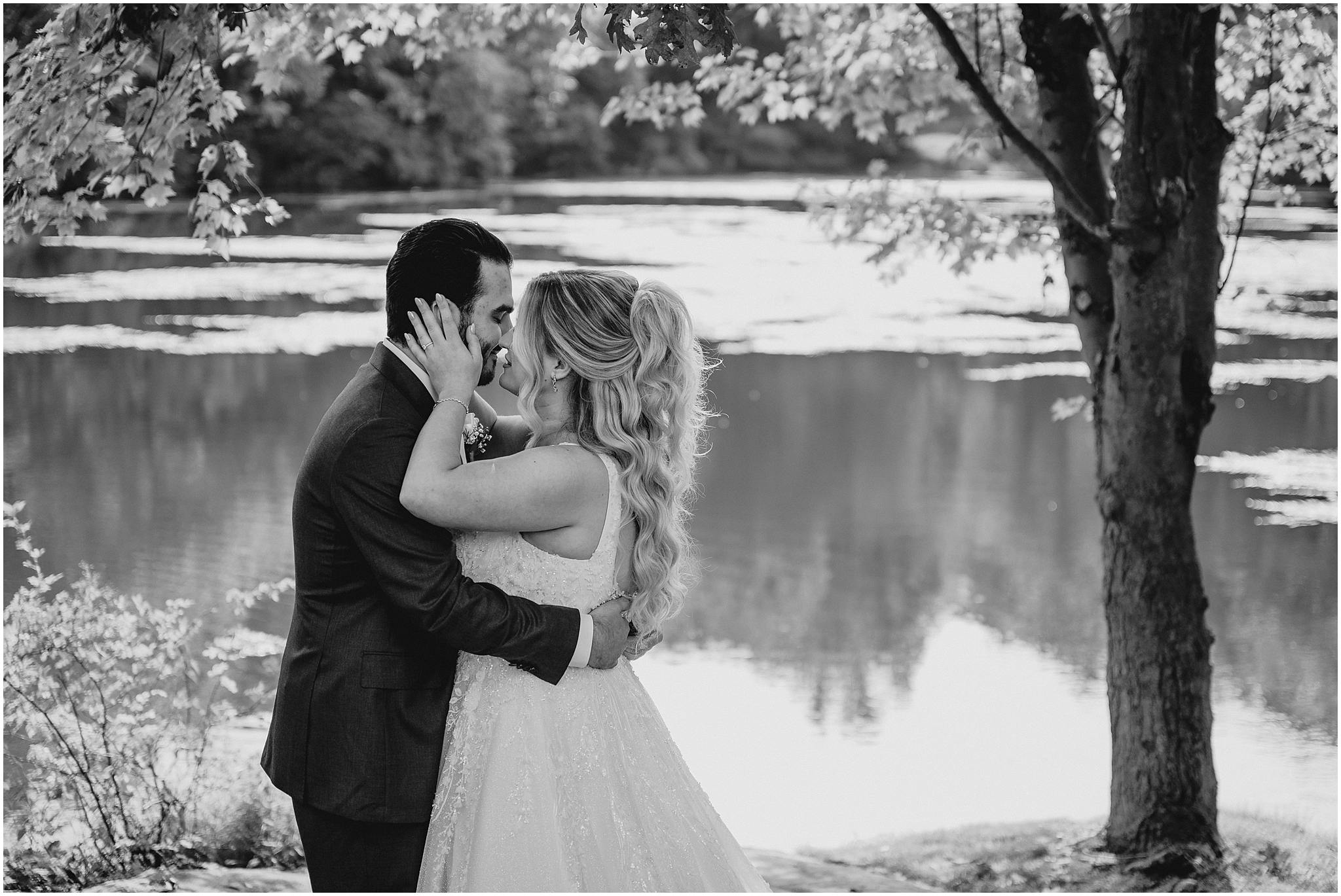 black and white photo of bride and groom leaning for a kiss by pond at the Refinery at Perona Farms