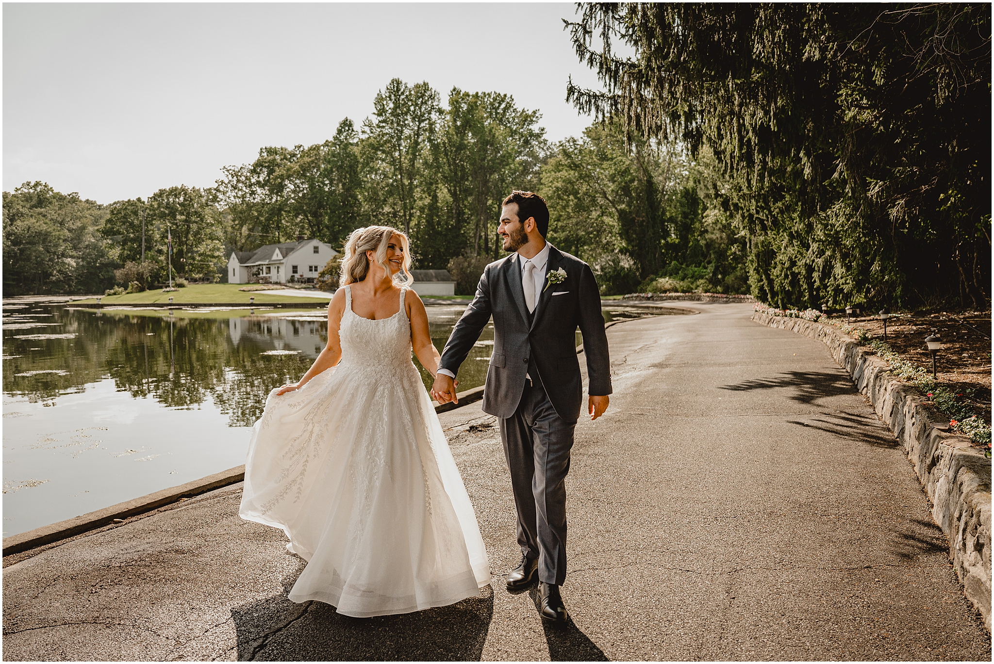 bride and groom hold hands walking along pond at the Refinery at Perona Farms