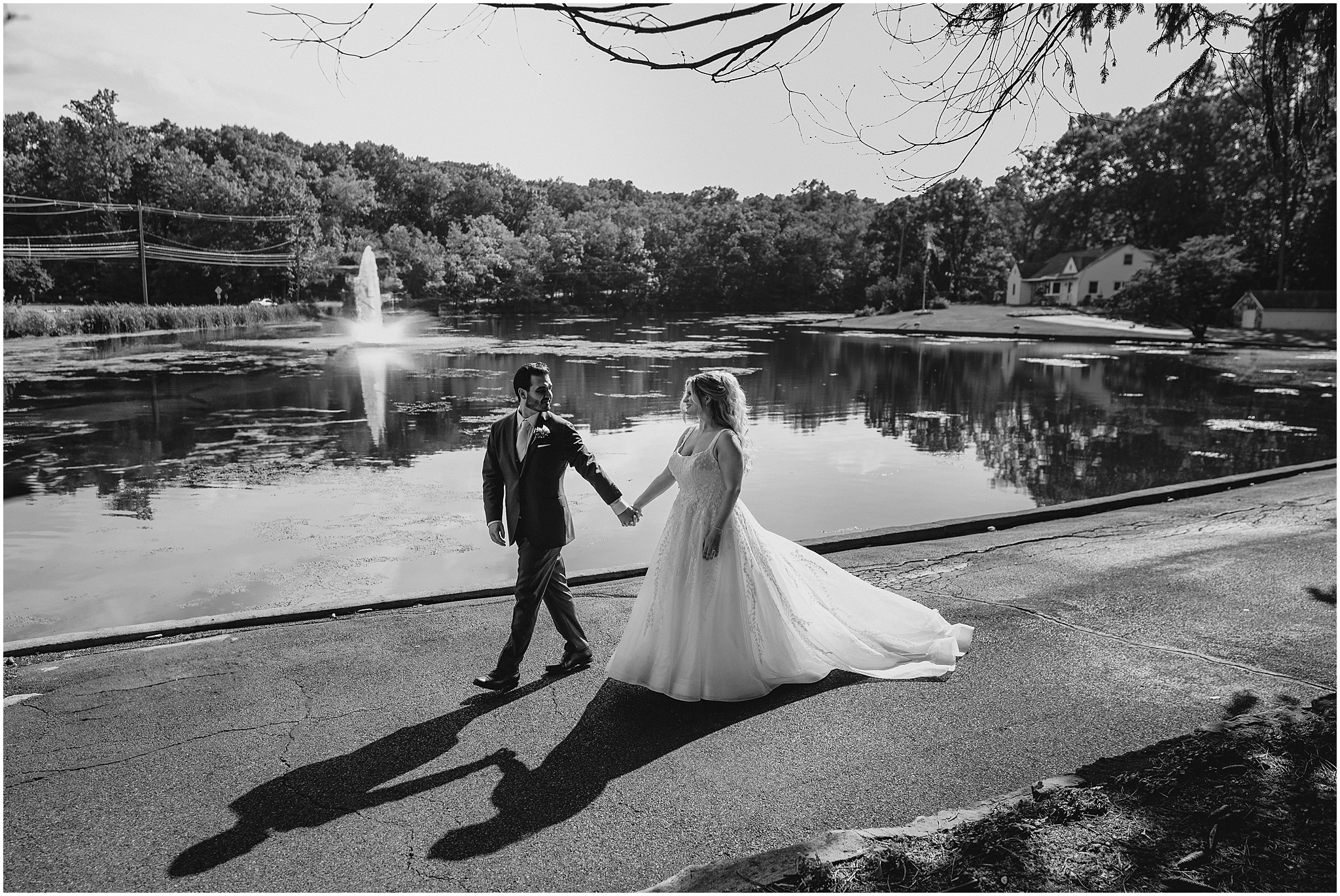 groom leads bride along path by pond at the Refinery at Perona Farms