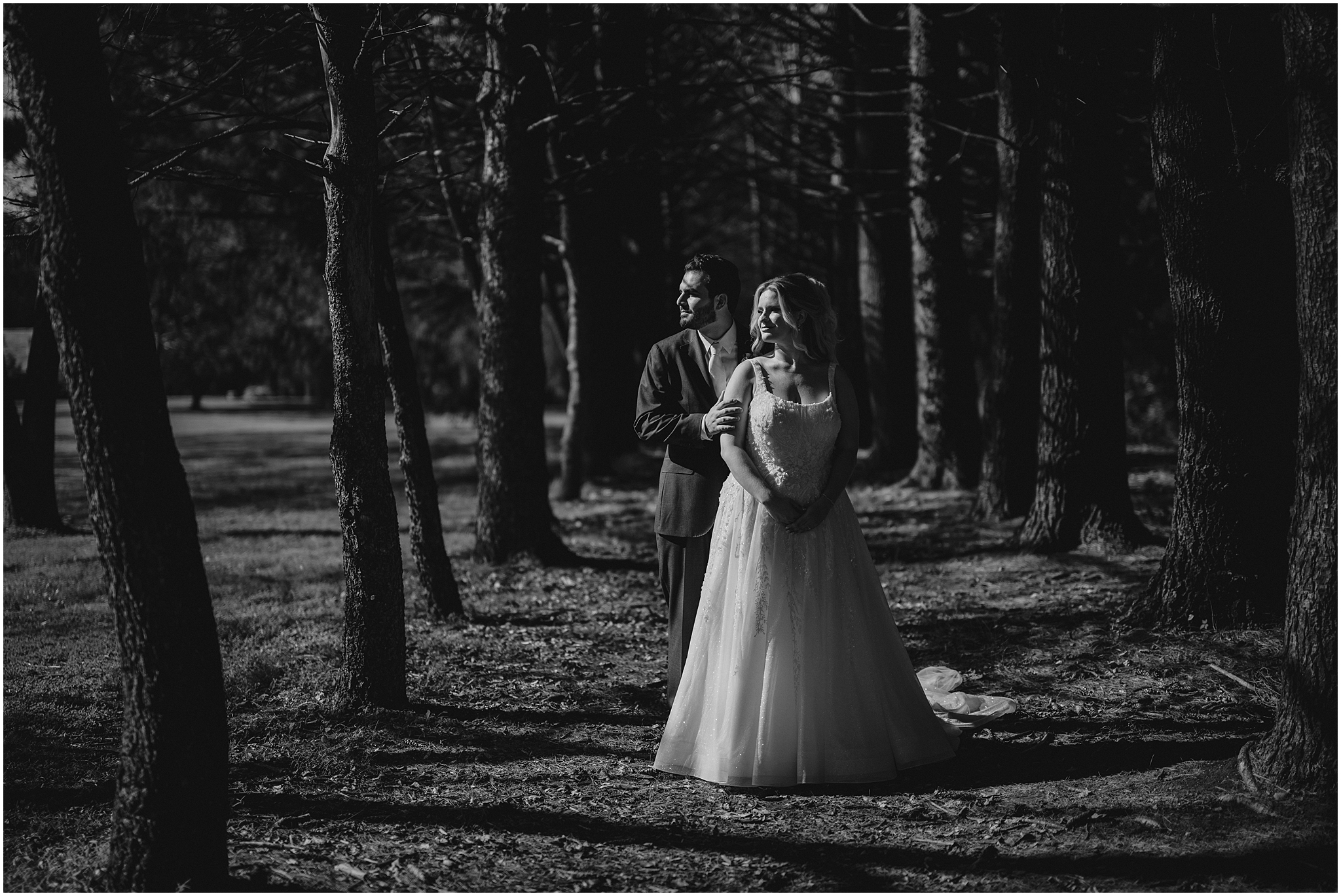 black and white photo of bride and groom standing between trees at the Refinery at Perona Farms