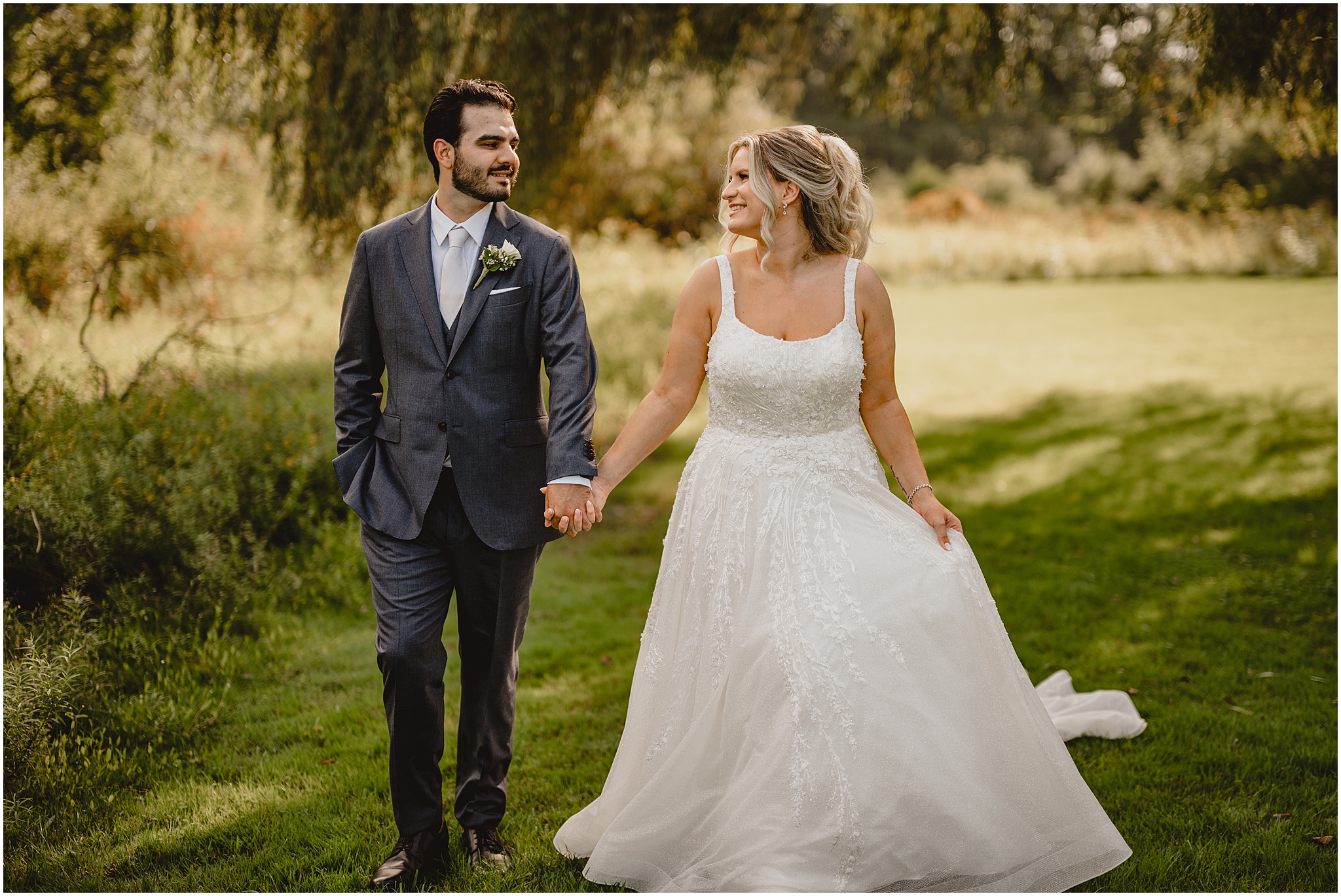 newlyweds hold hands smiling together walking through field in Andover NJ