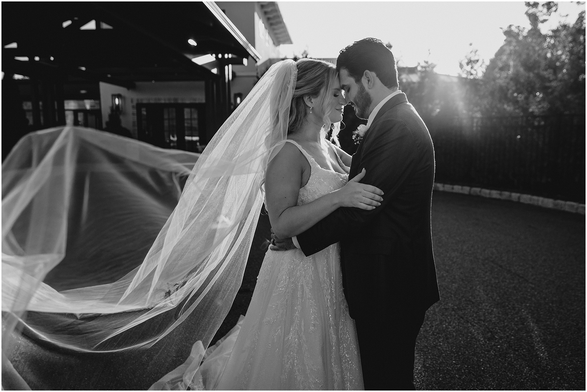 newlyweds lean heads together with bride's veil floating behind them