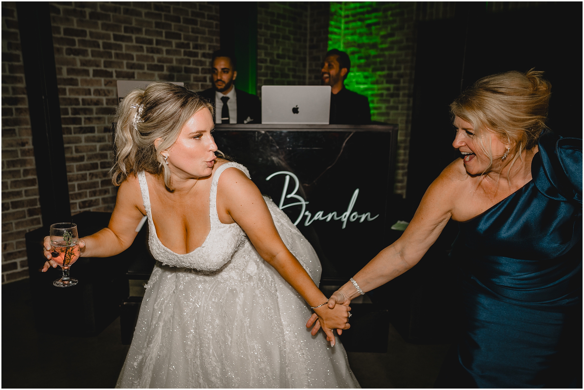 bride and mom hold hands dancing in front of DJ booth