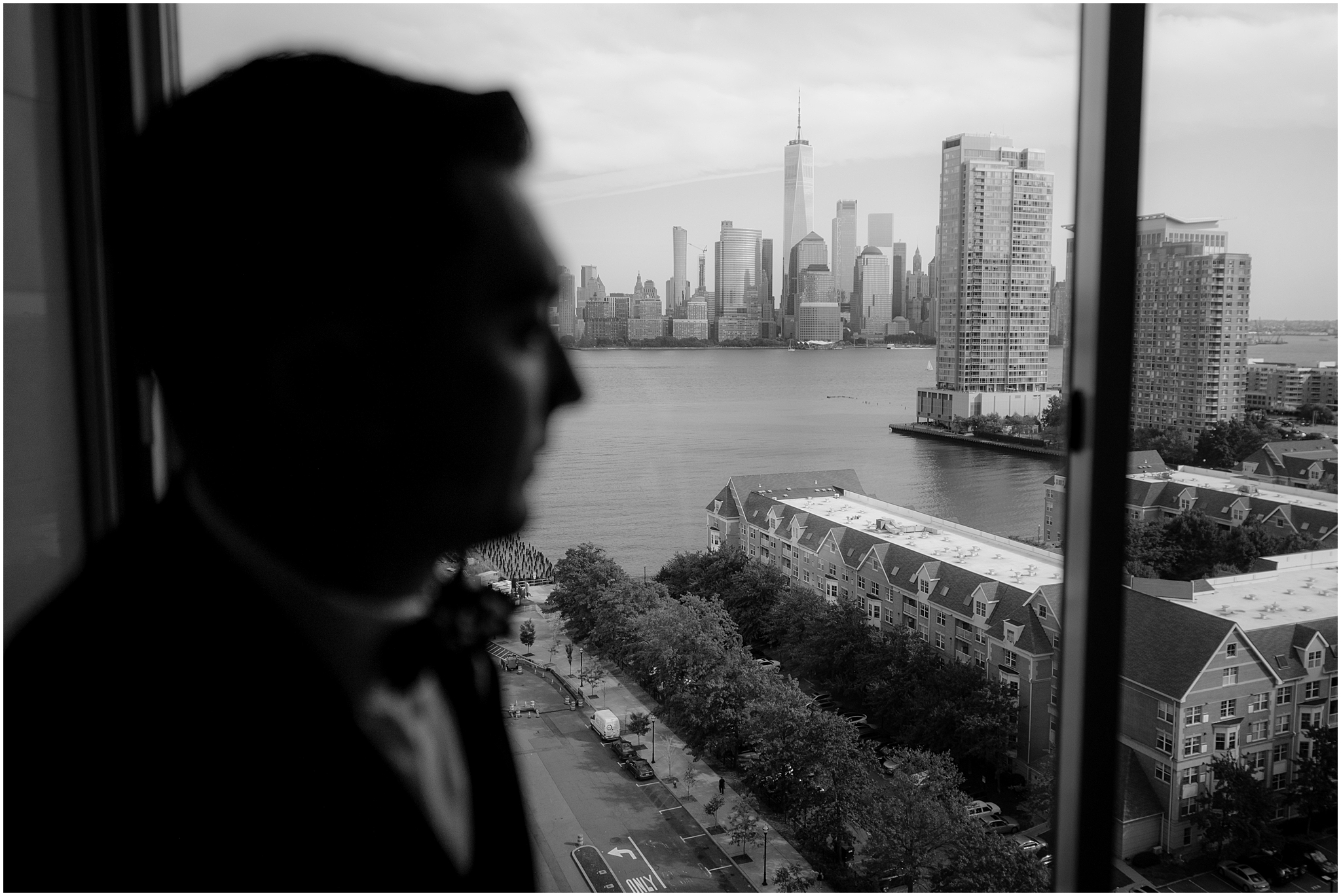 groom looks out the window his NJ hotel room at NYC skyline