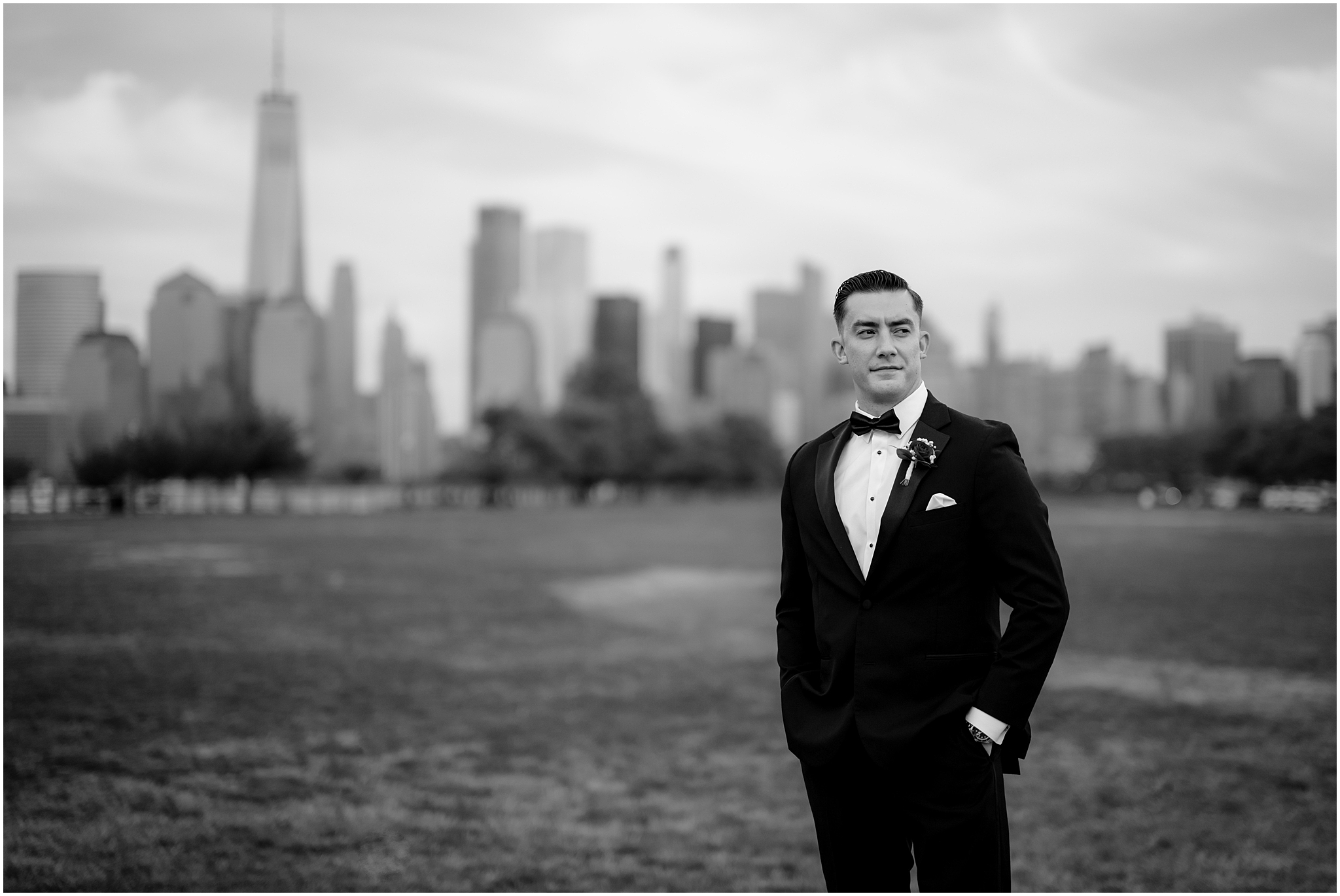 black and white photo of groom standing on lawn with Manhattan skyline behind him