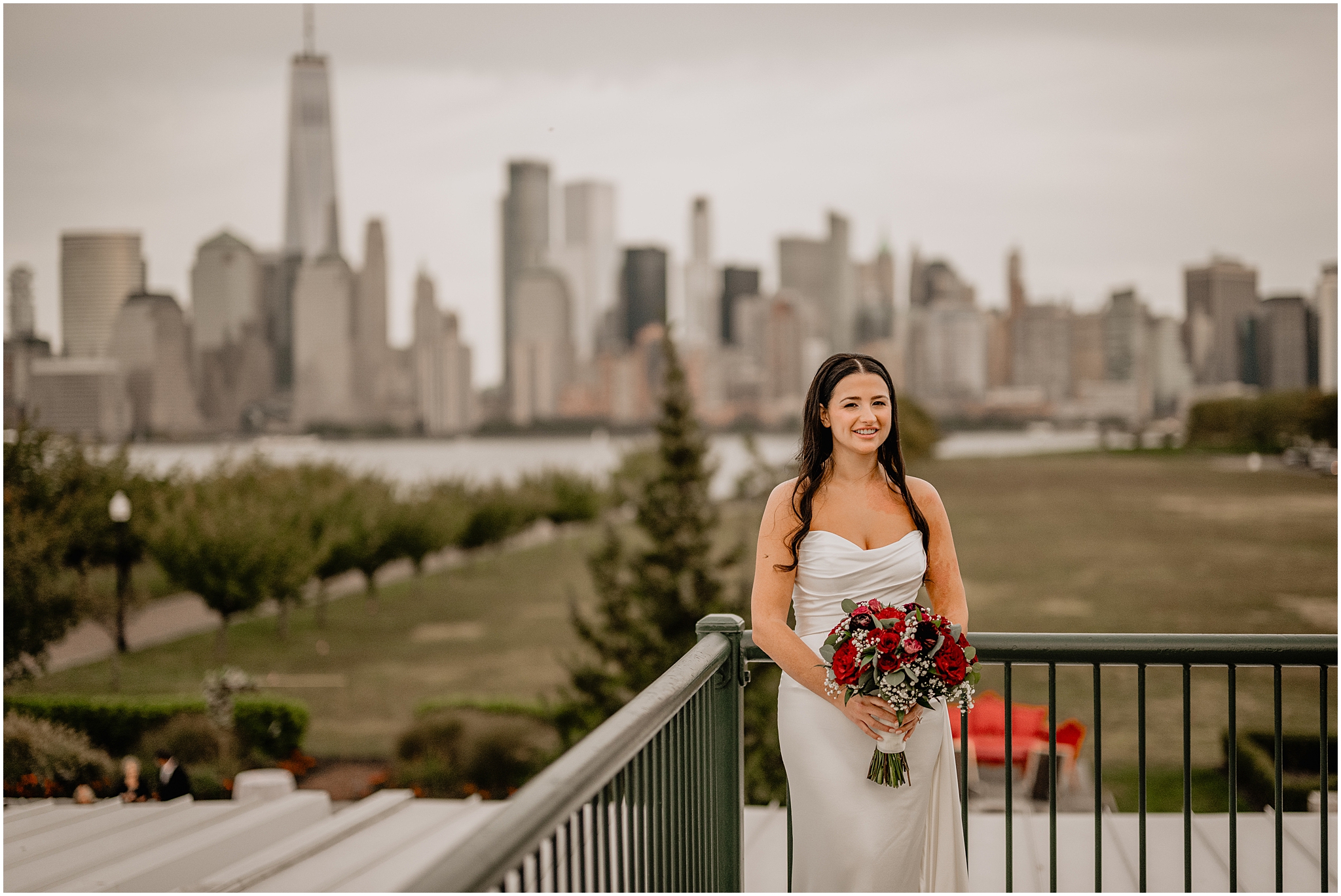 bride stands on balcony at the Liberty House holding bouquet of red roses in strapless wedding gown