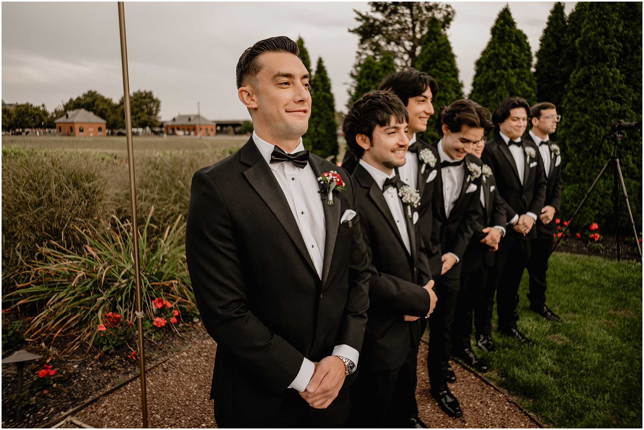 groom and groomsmen laugh watching flower boys walking down aisle 