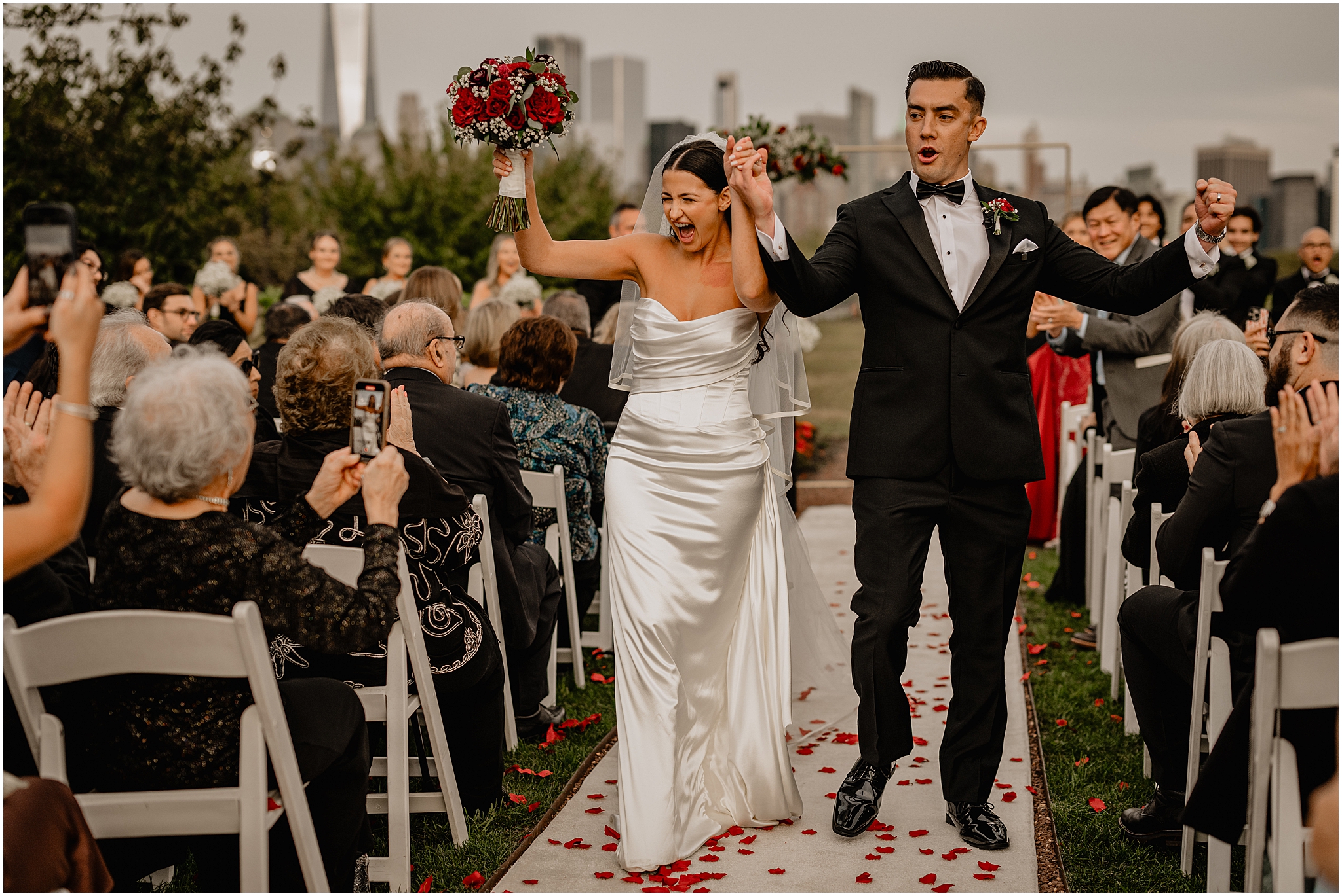 newlyweds cheer walking up aisle covers in red rose petals at the Liberty House