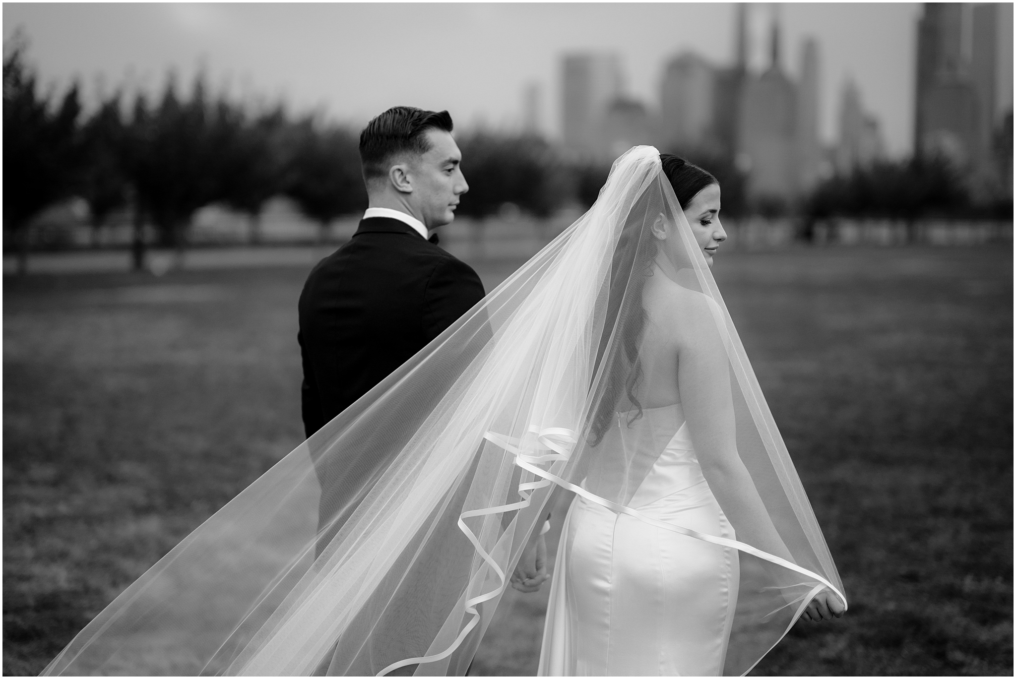 bride pulls veil around her shoulder while walking holding hands with groom in New Jersey