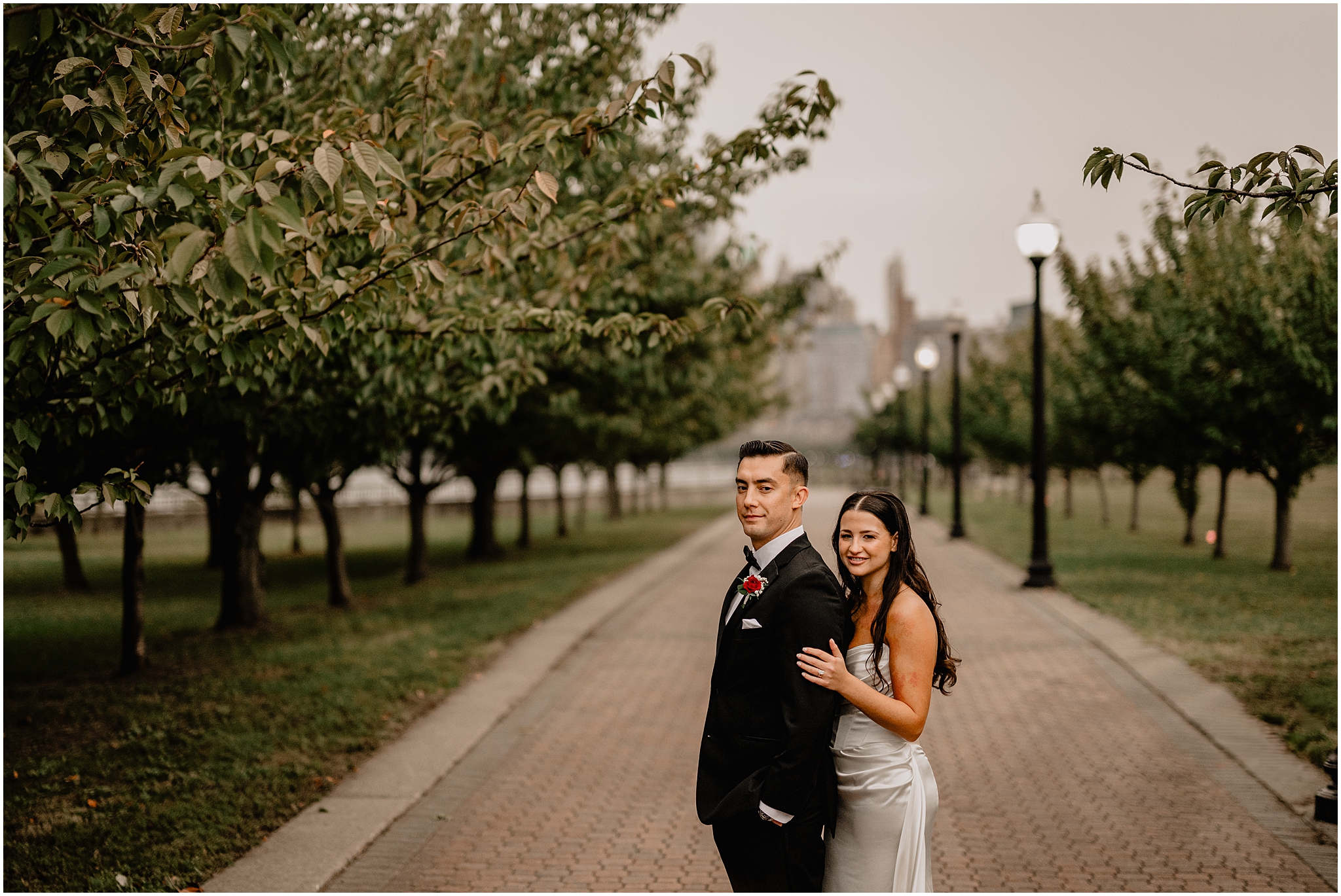 bride stands behind groom hugging him during wedding photos in Jersey City