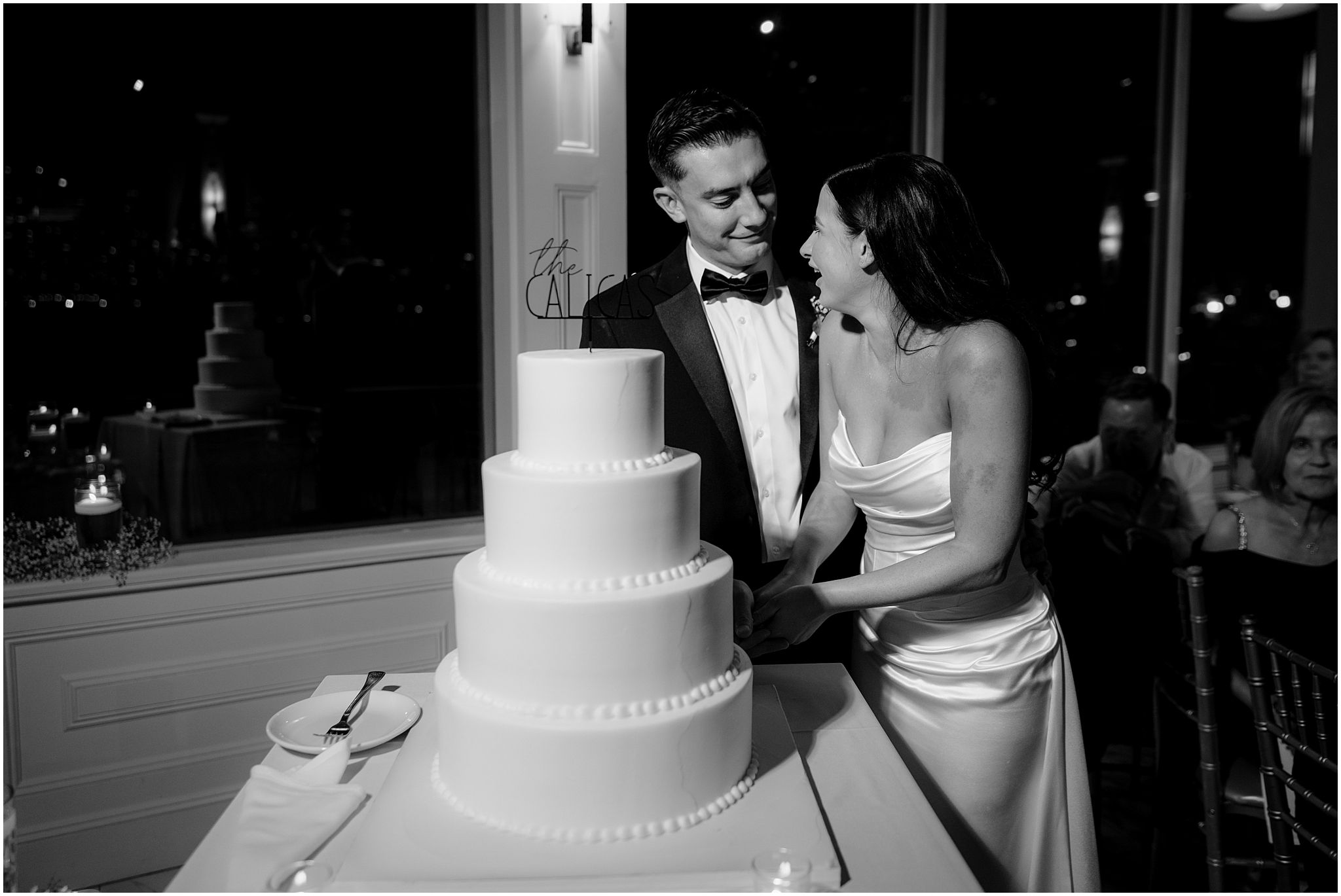 bride and groom smile at each other cutting wedding cake during Jersey City wedding reception