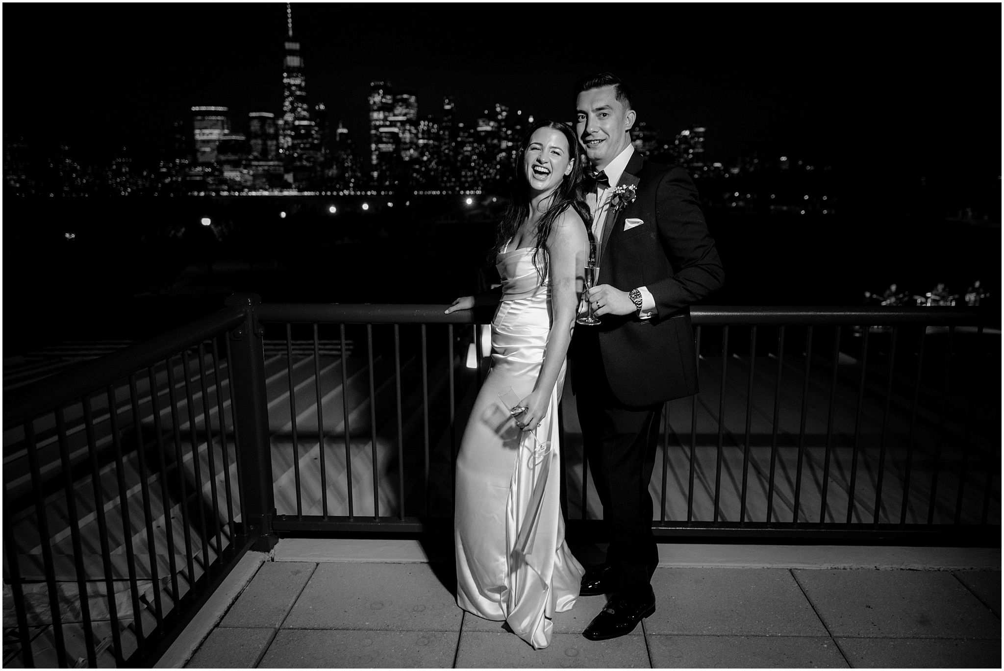 groom and bride hold glasses of champagne hugging together in front of Manhattan skyline on patio at the Liberty House 