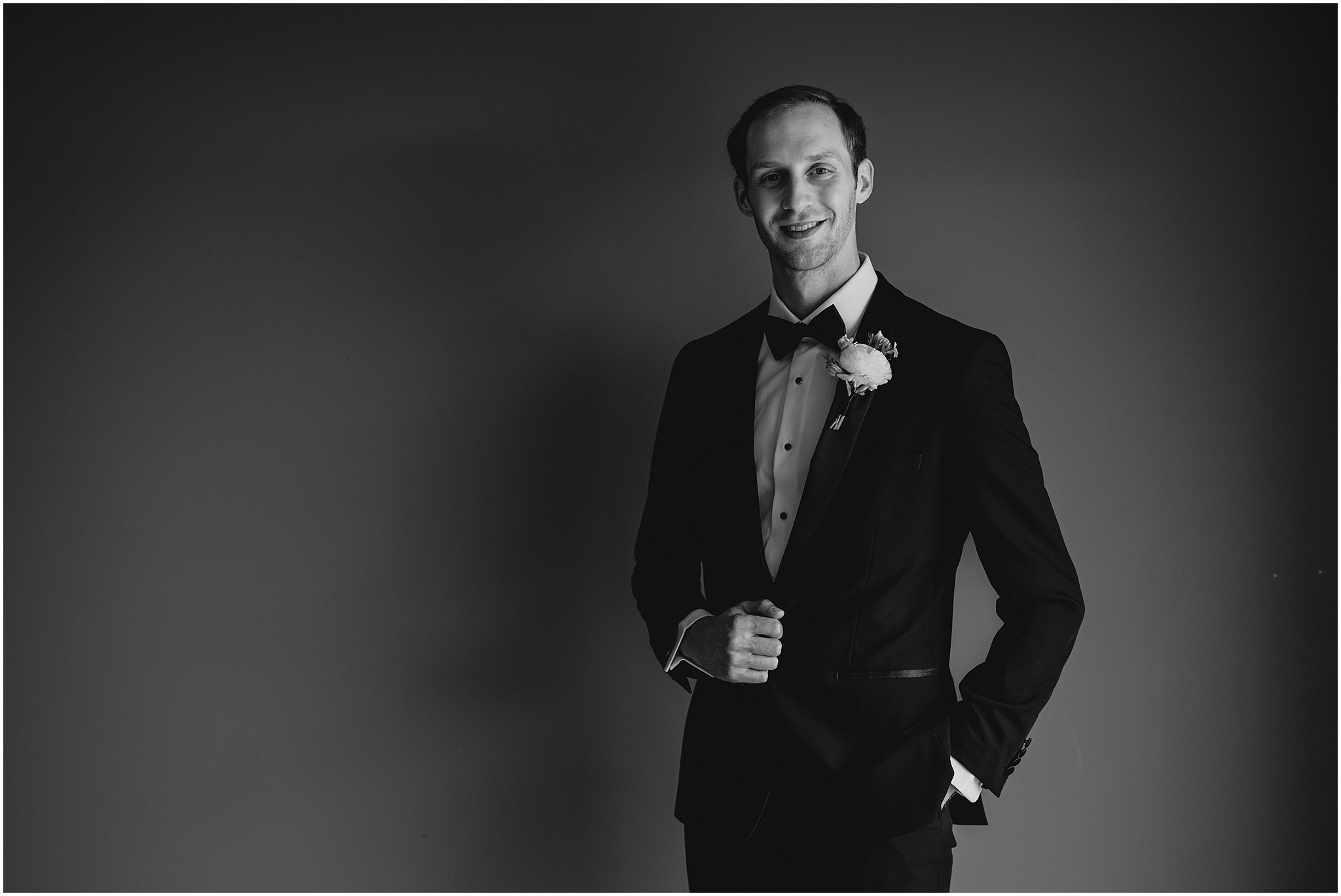 black and white photo of groom holding lapel of black suit jacket