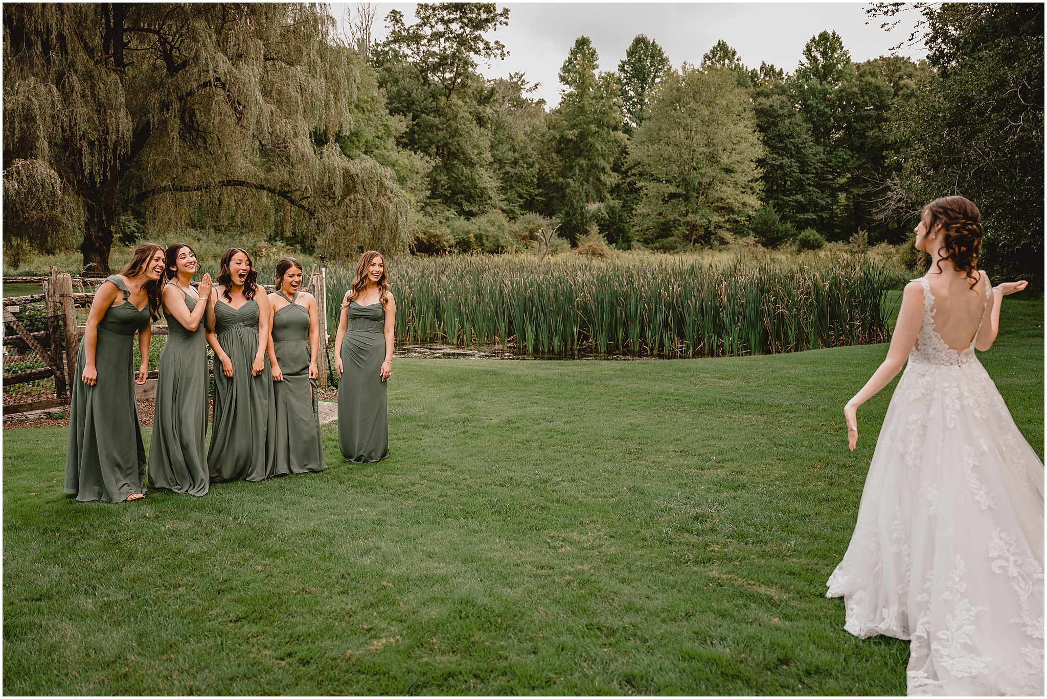 bride shows off wedding dress to bridesmaids in sage green gowns by pond at the Reserve at Perona Farms
