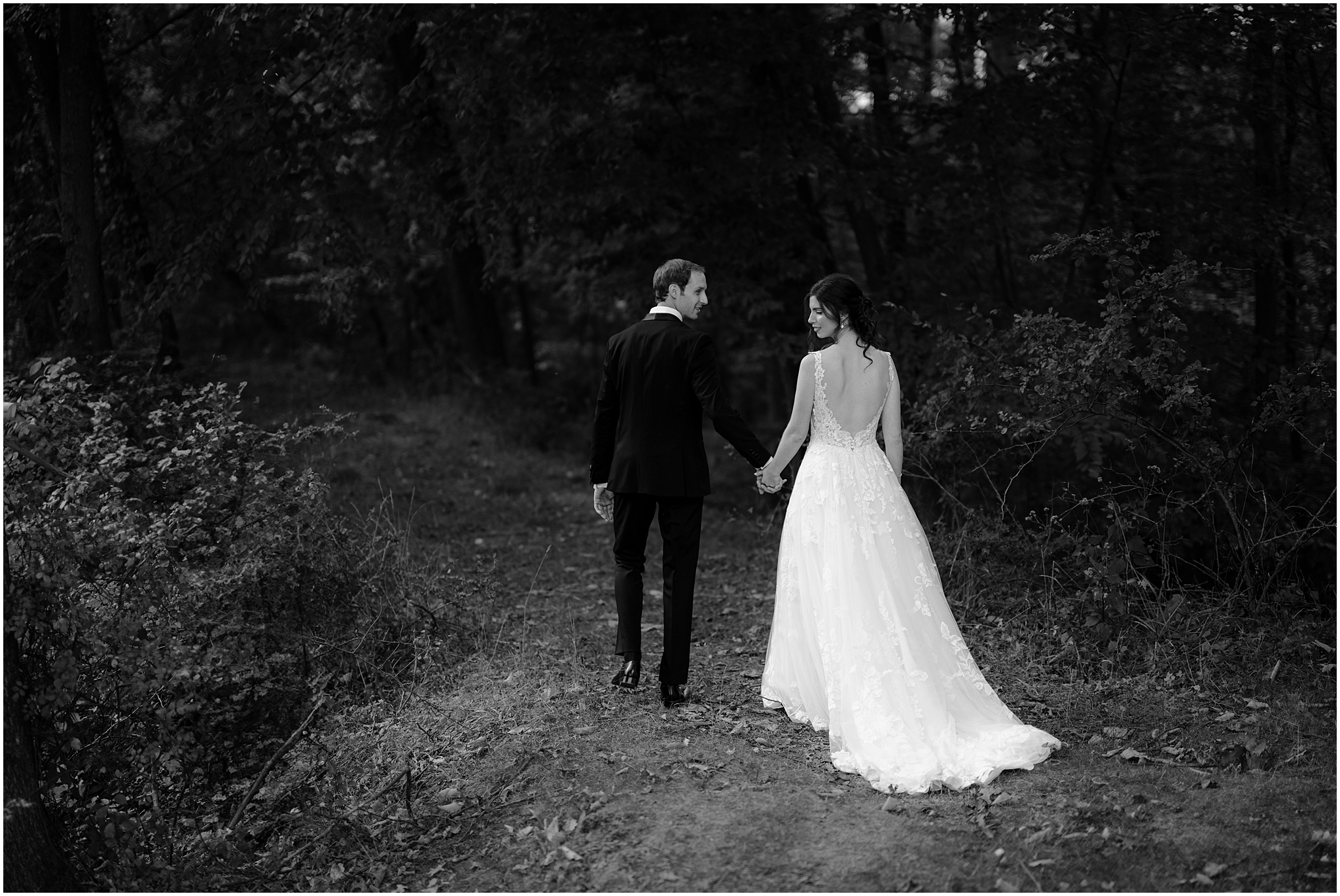bride and groom hold hands walking down pathway in woods at the Reserve at Perona Farms