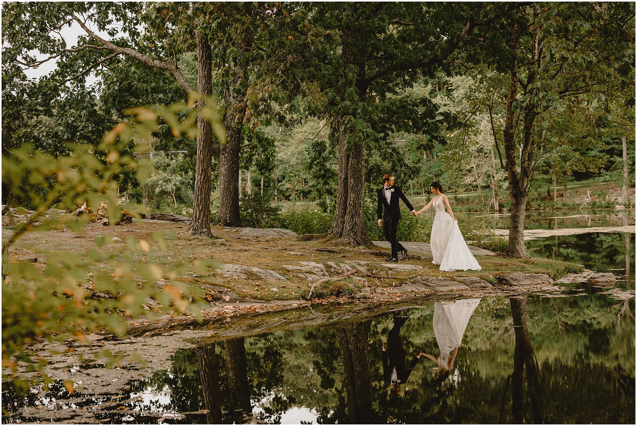 groom holds bride's hand leading her across small hill by pond at the Reserve at Perona Farms