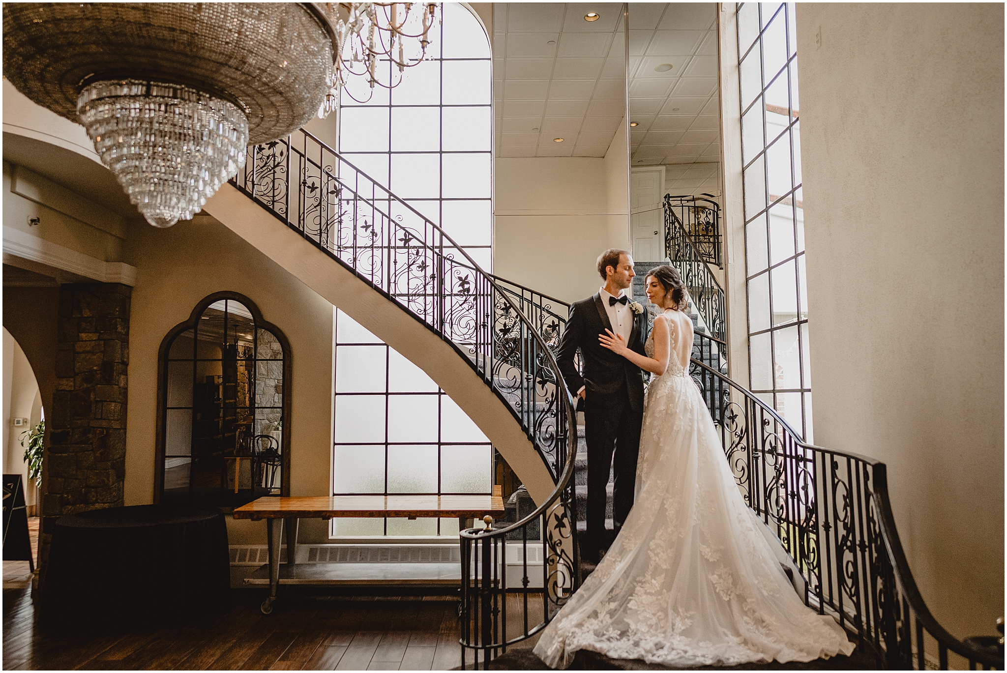 groom stands on staircase with bride next to him with her train laid out behind them on the steps