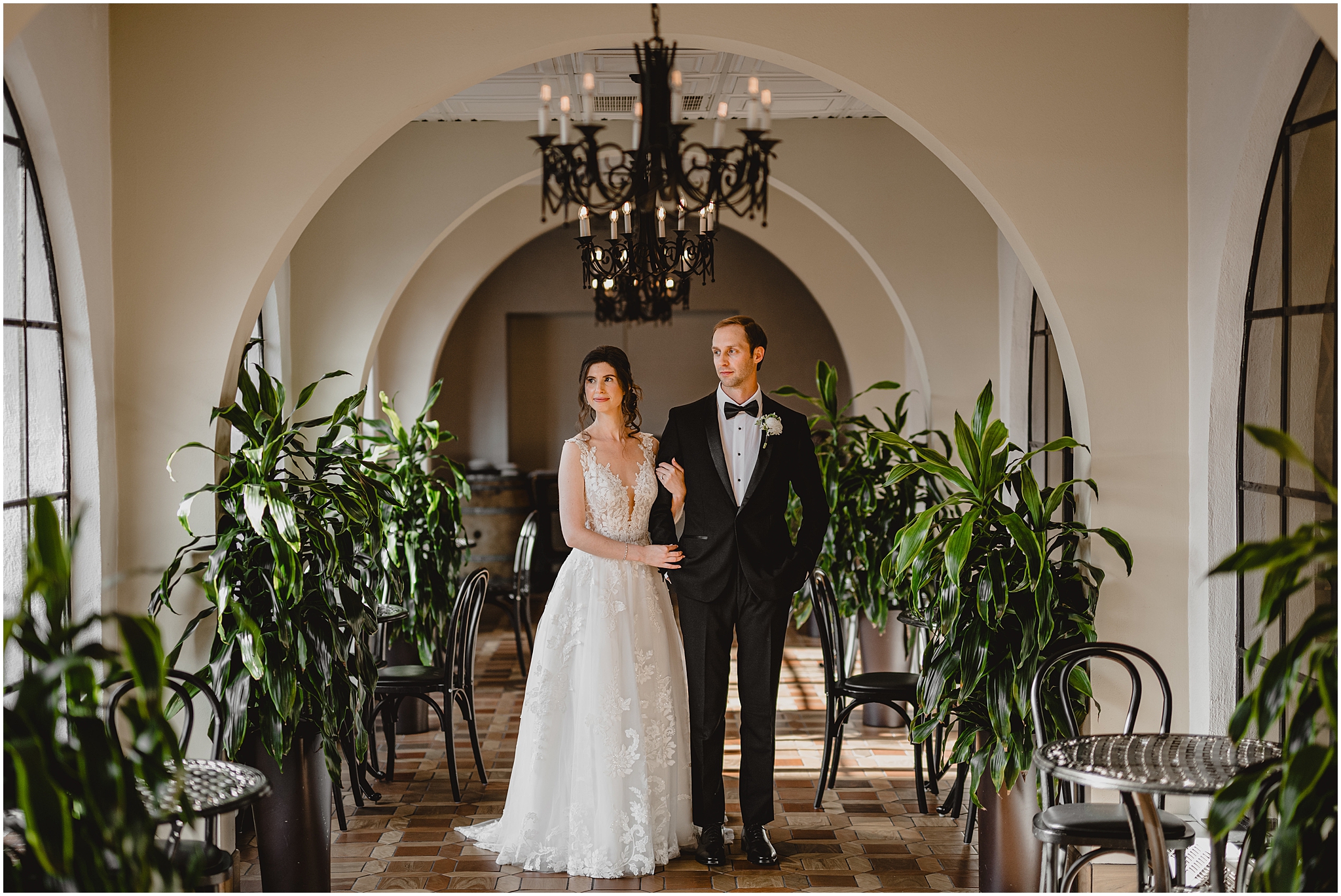 bride holds groom's arm standing in hallway surrounded by green plants at the Reserve at Perona Farms