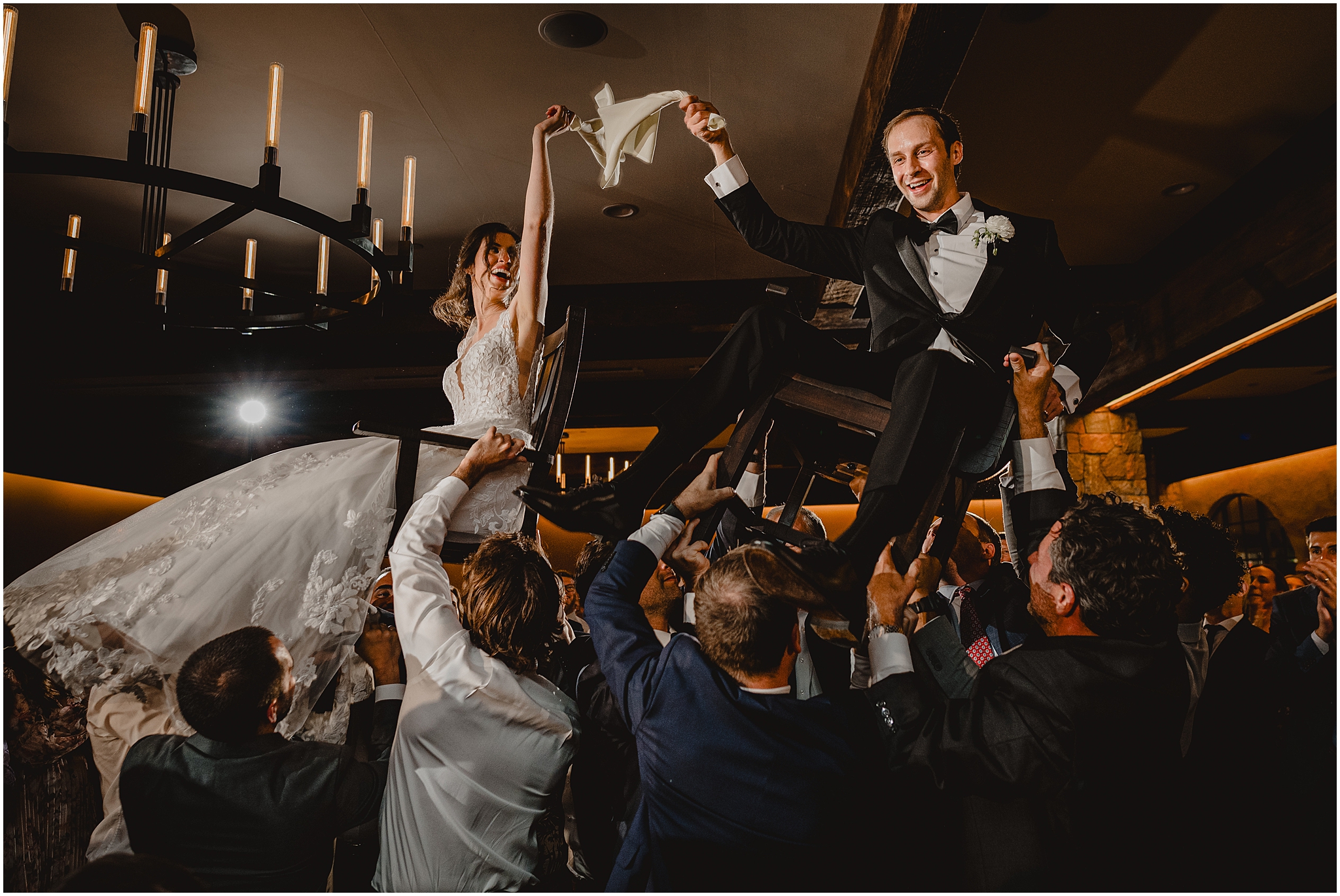 bride and groom hold white napkin between them while being lifted in the air during the hora