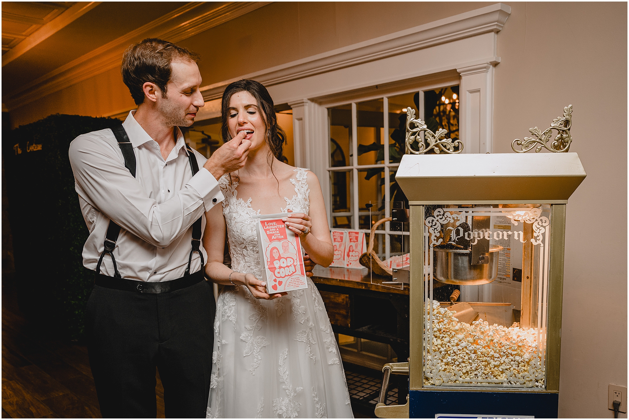 groom feeds bride popcorn standing next to popcorn maker for wedding reception 