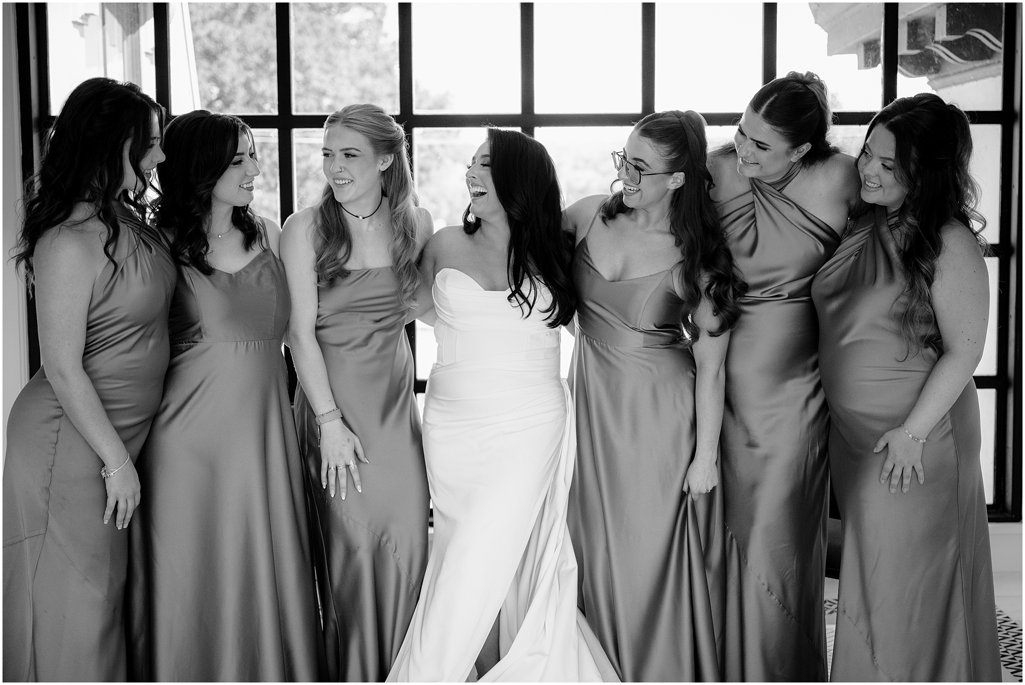 bride laughs hugging bridesmaids in mismatched satin gowns