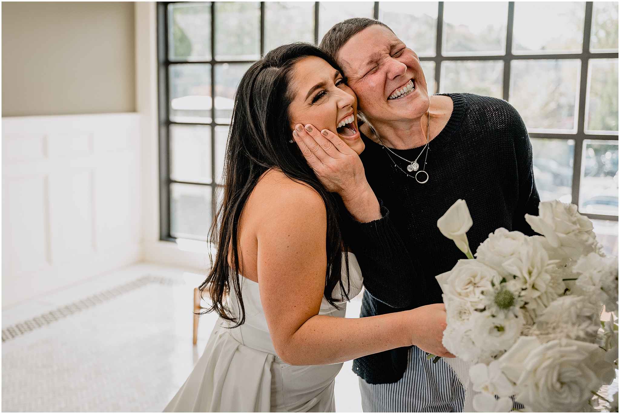 woman holds bride's chin laughing during first look in the lobby