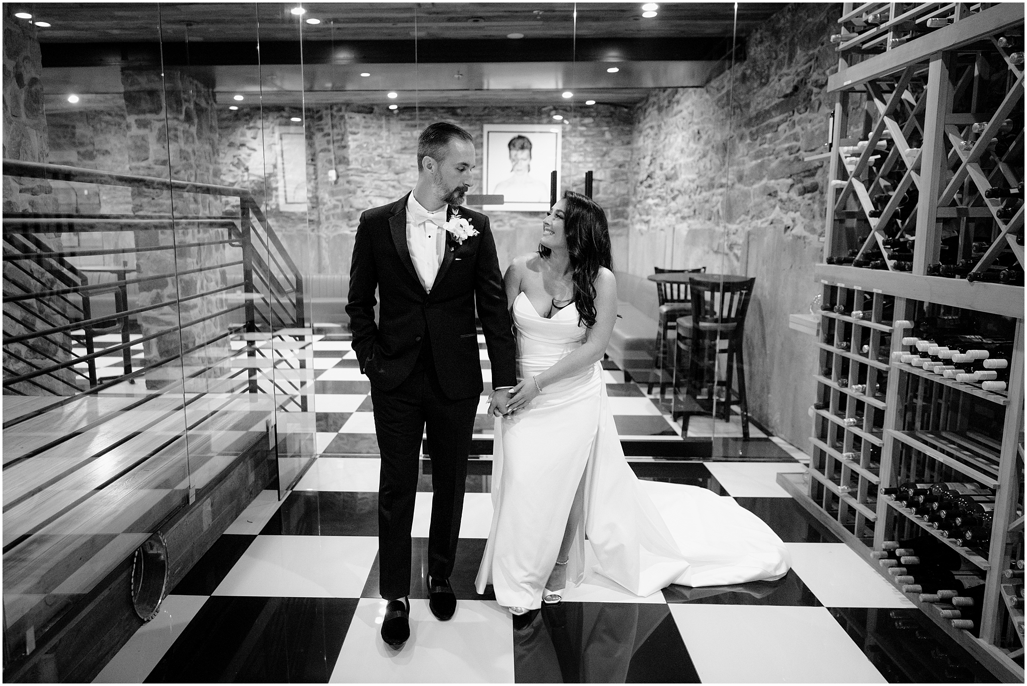 bride and groom hold hands walking through wine cellar in front of photo of David Bowie 
