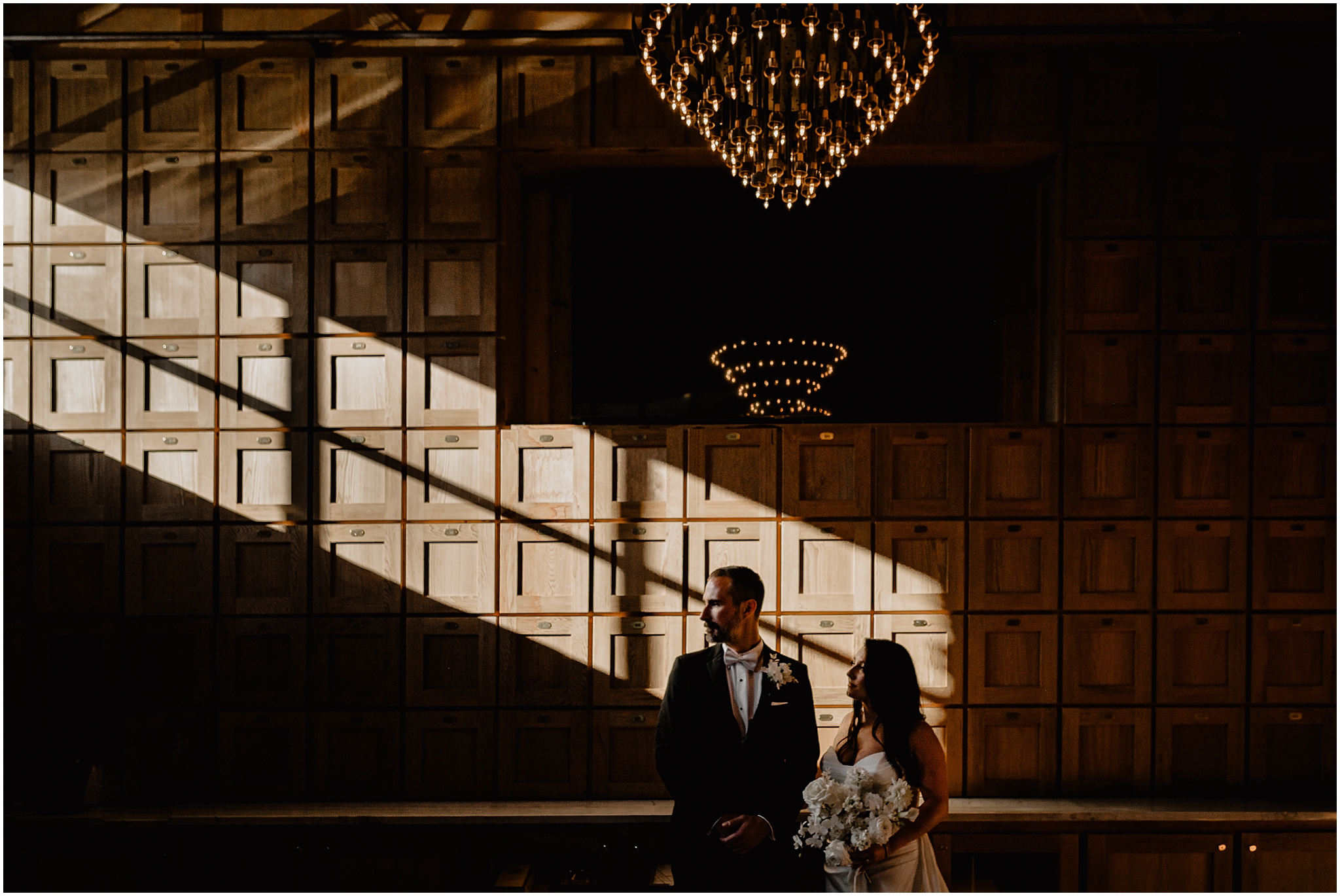 bride and groom stand in front of wood paneled wall at The Logan Inn in strip of sunlight 
