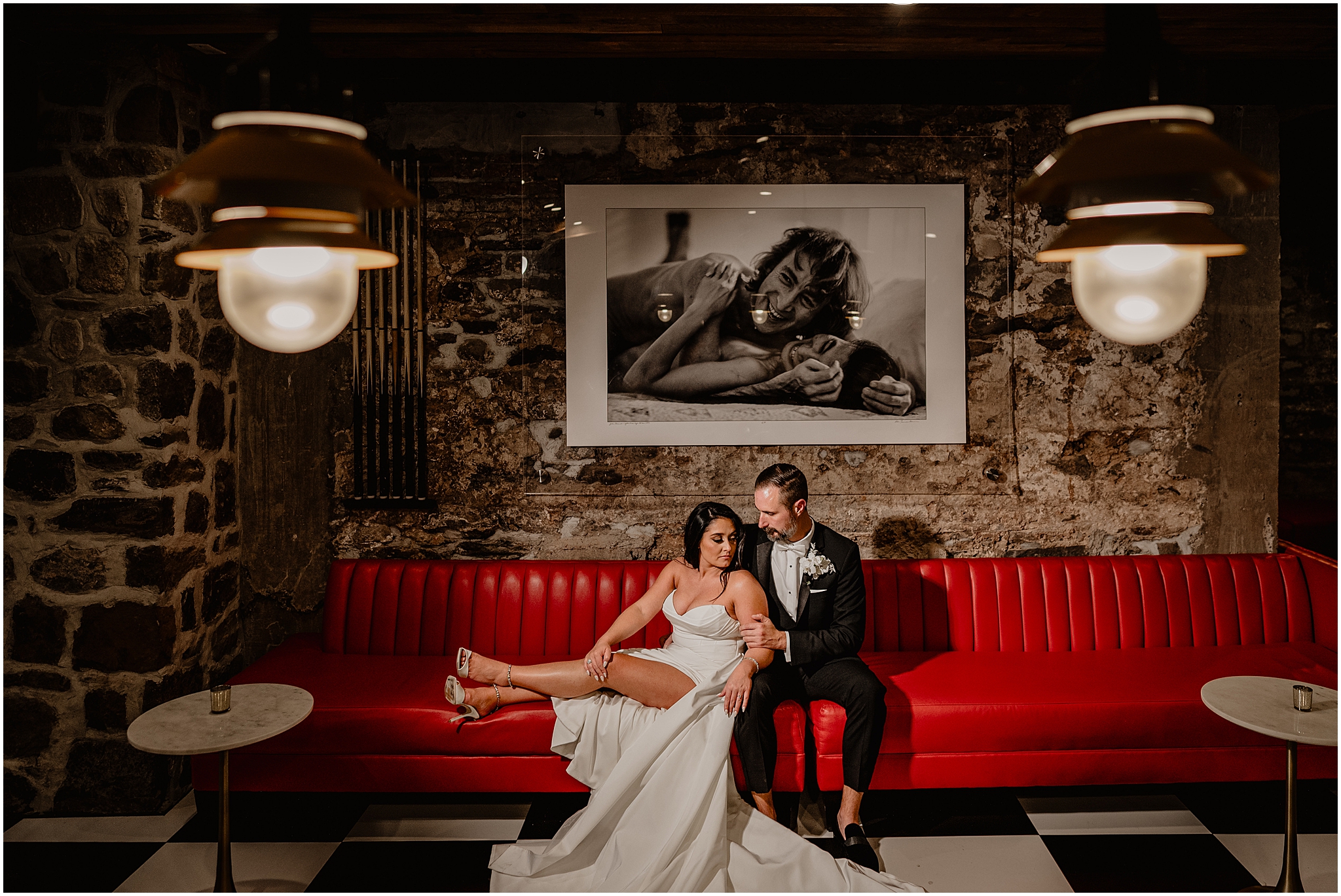 bride and groom sit together on red leather couch under black and white photo in New Hope PA venue