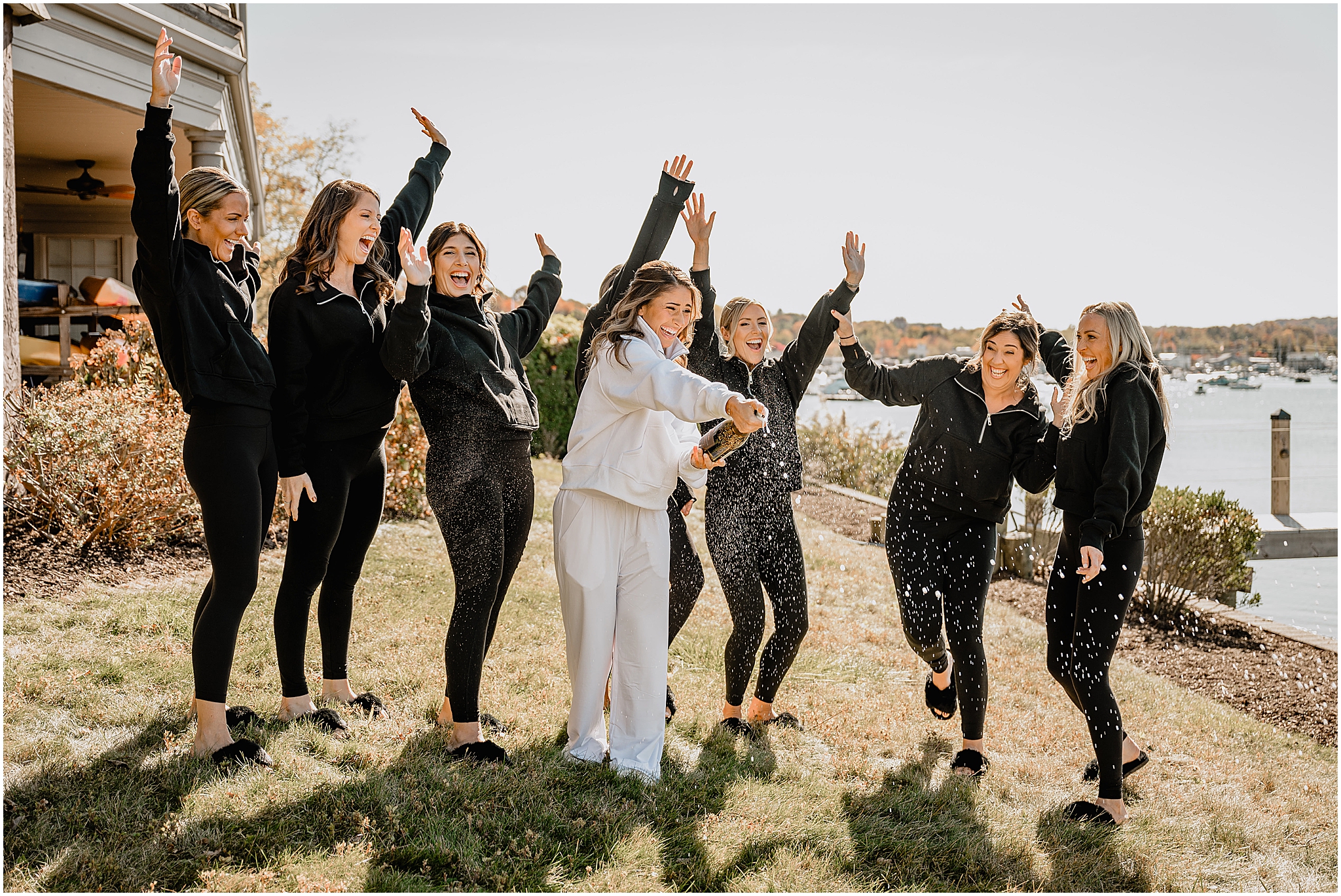 bride pops champagne standing outside the Waters Edge at Centerport with bridesmaids in matching black and white track suits 