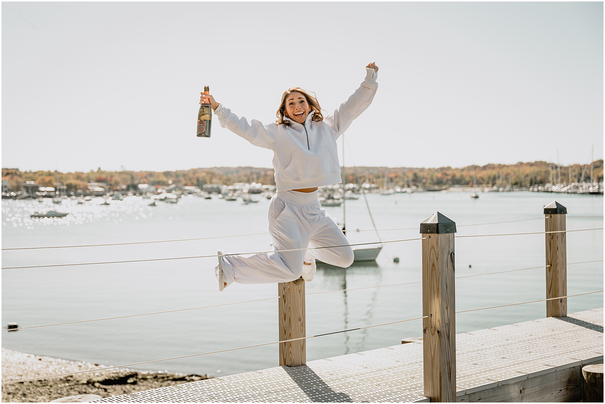 bride jumps in the air on the dock at the Waters Edge at Centerport in white lounge set