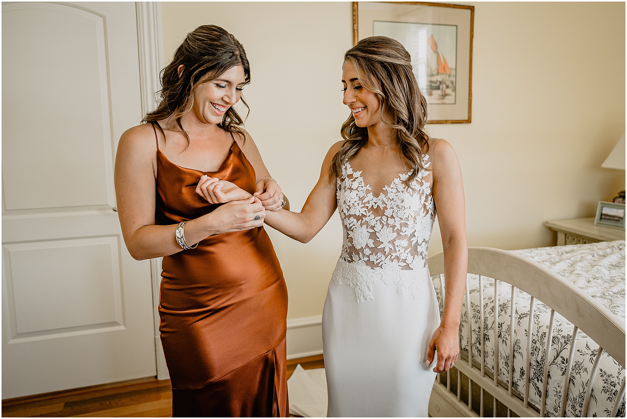 bridesmaid in orange satin gown helps bride with bracelet on the morning of her wedding