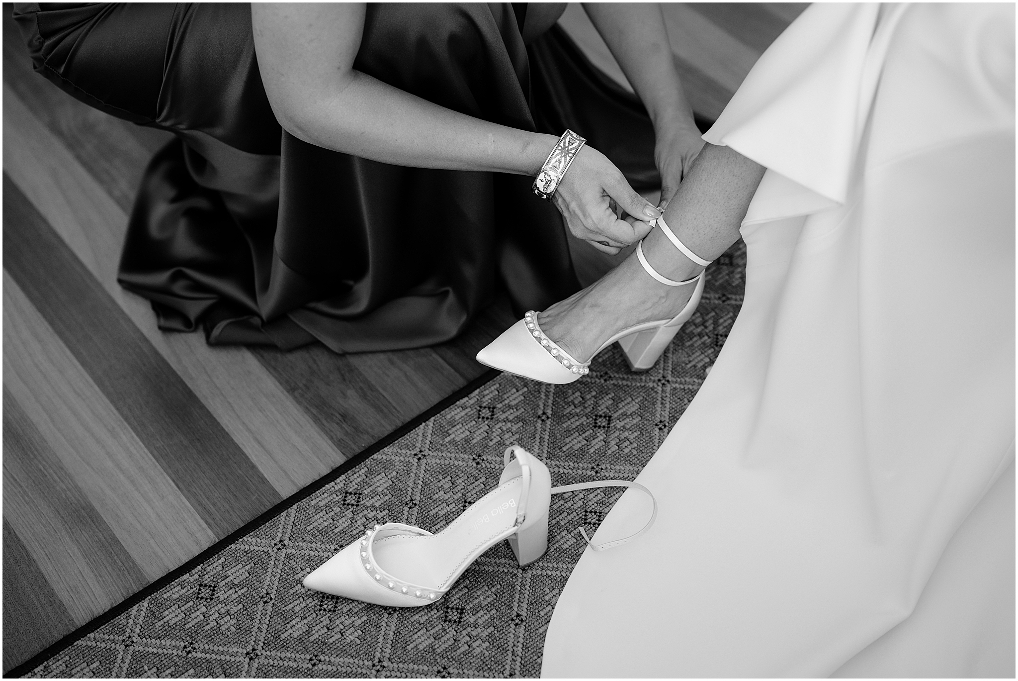 woman kneels adjusting strap on bride's heels