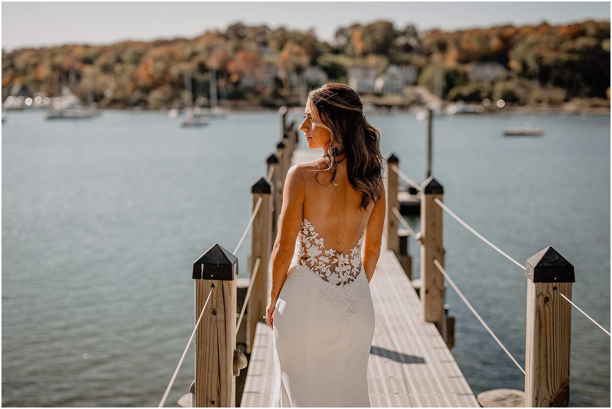 bride looks over shoulder standing on dock in wedding gown lace detailing around bodice