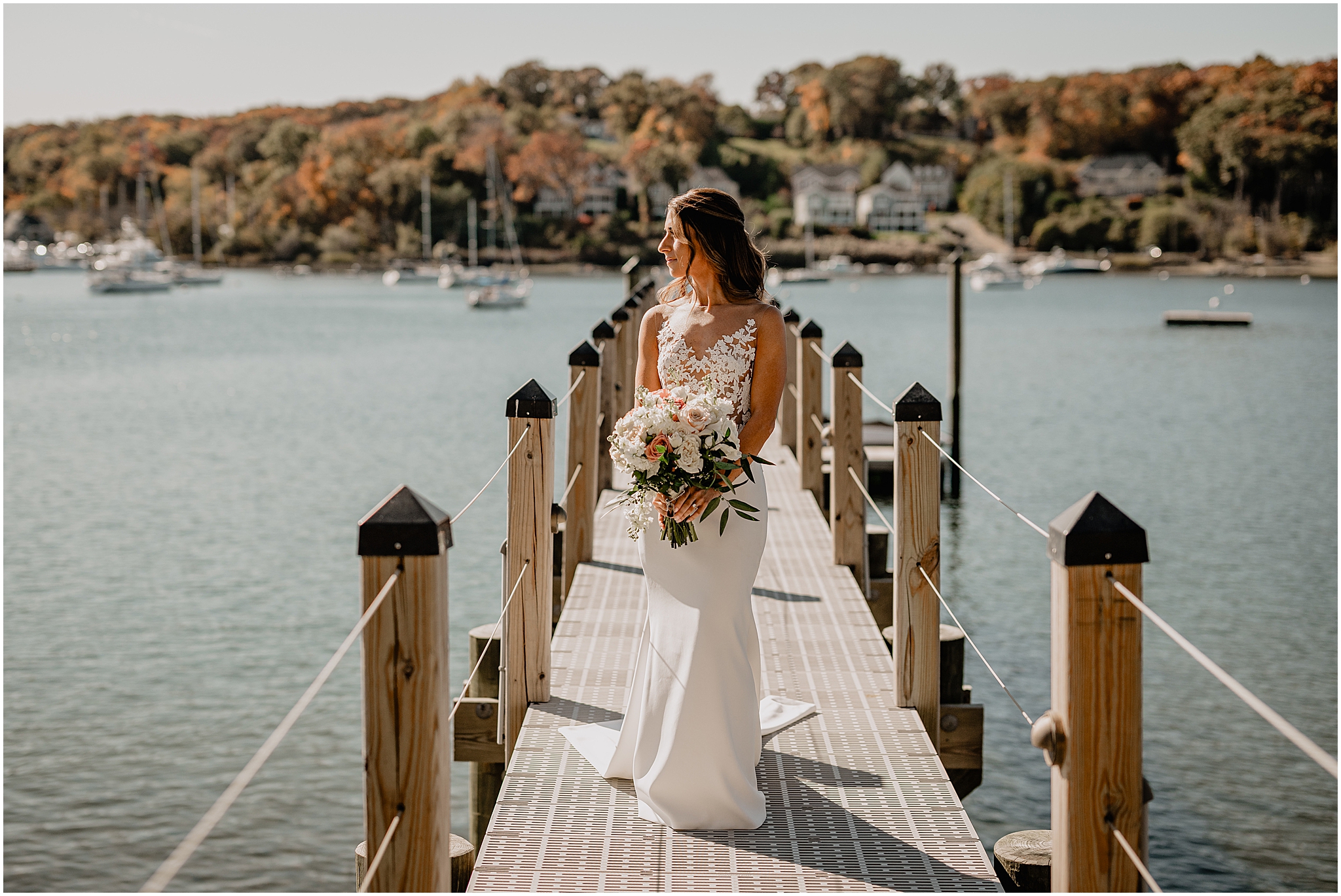 bride stands on dock on Long Island holding bouquet of pink and white flowers at the Waters Edge at Centerport