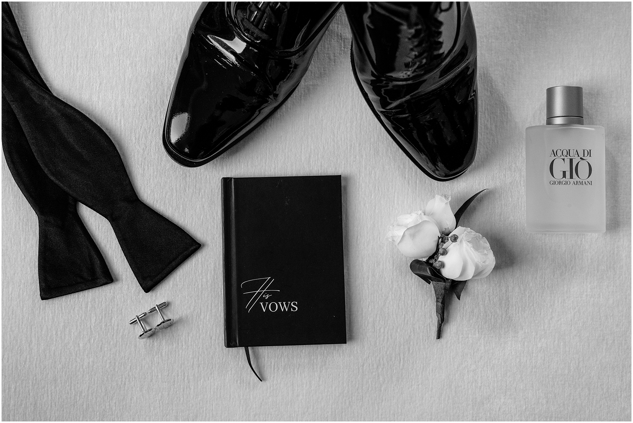 black and white photo of groom's black shoes, bow tie and vow book