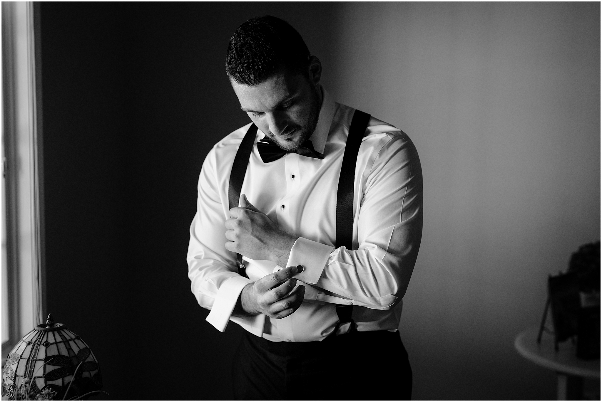 groom adjusts cufflinks standing in suspenders and white shirt 