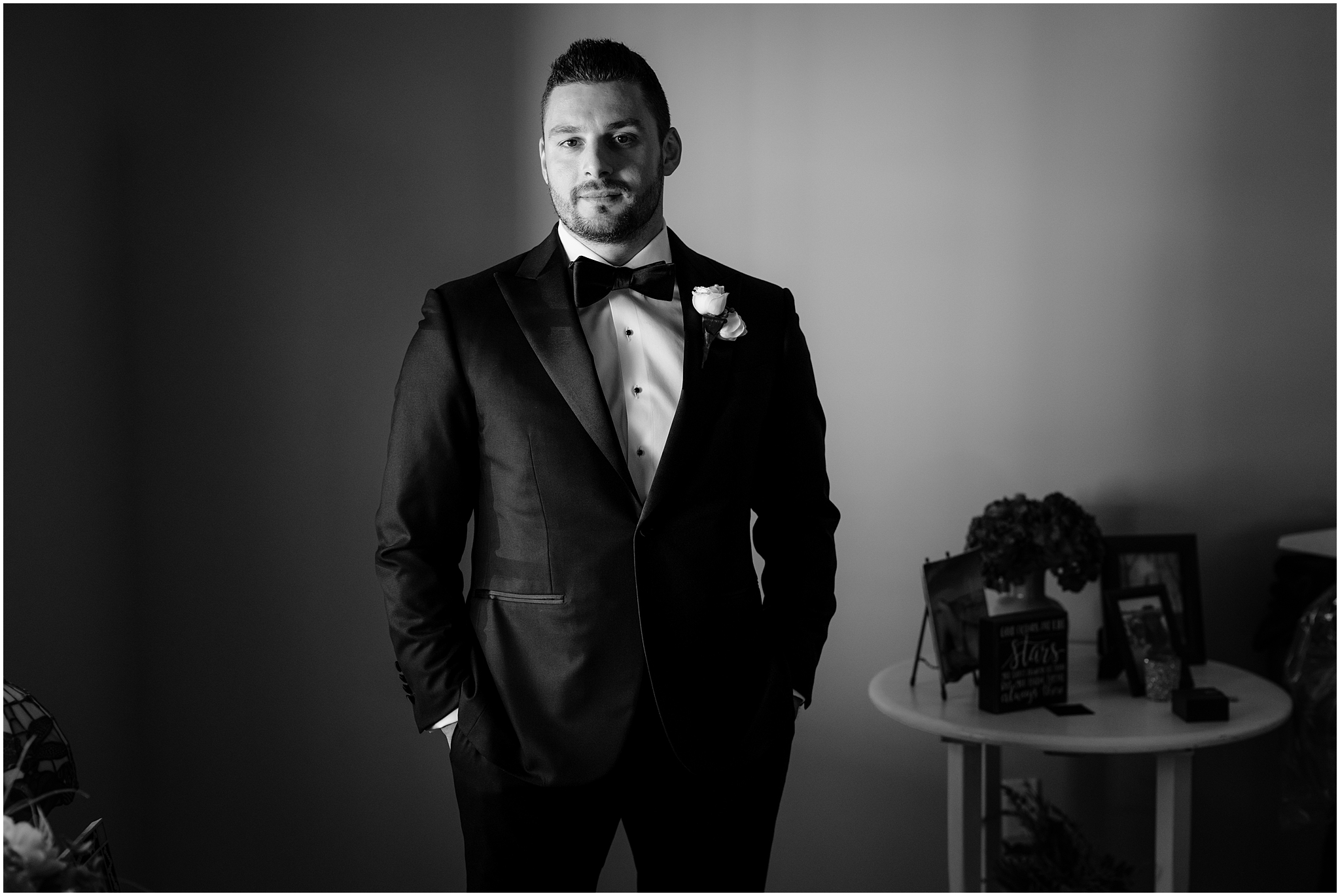 groom stands with hands in pocket of his black suit before Long Island wedding