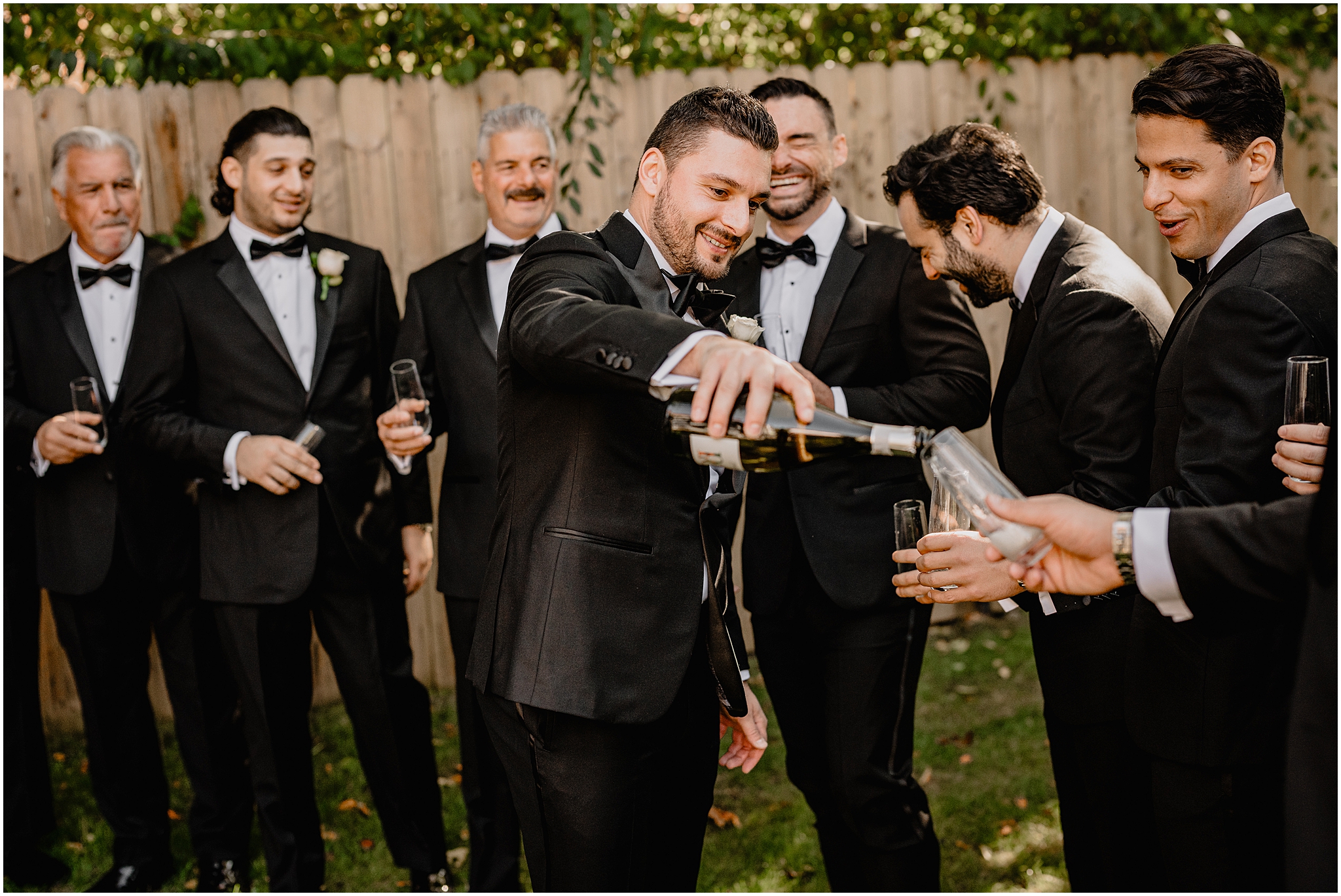 groom pours champagne for groomsmen during prep in backyard of Long Island home