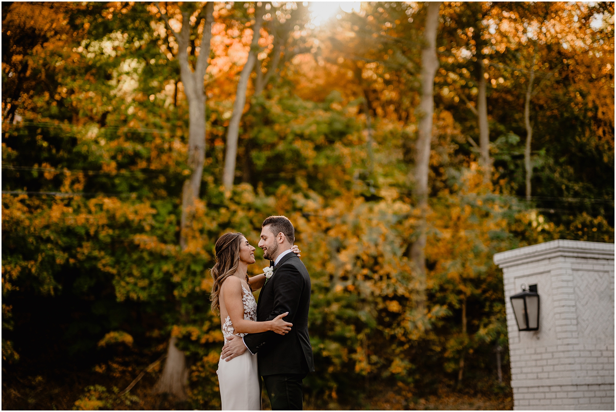 bride and groom hug in front of fall colored leaves on Long Island