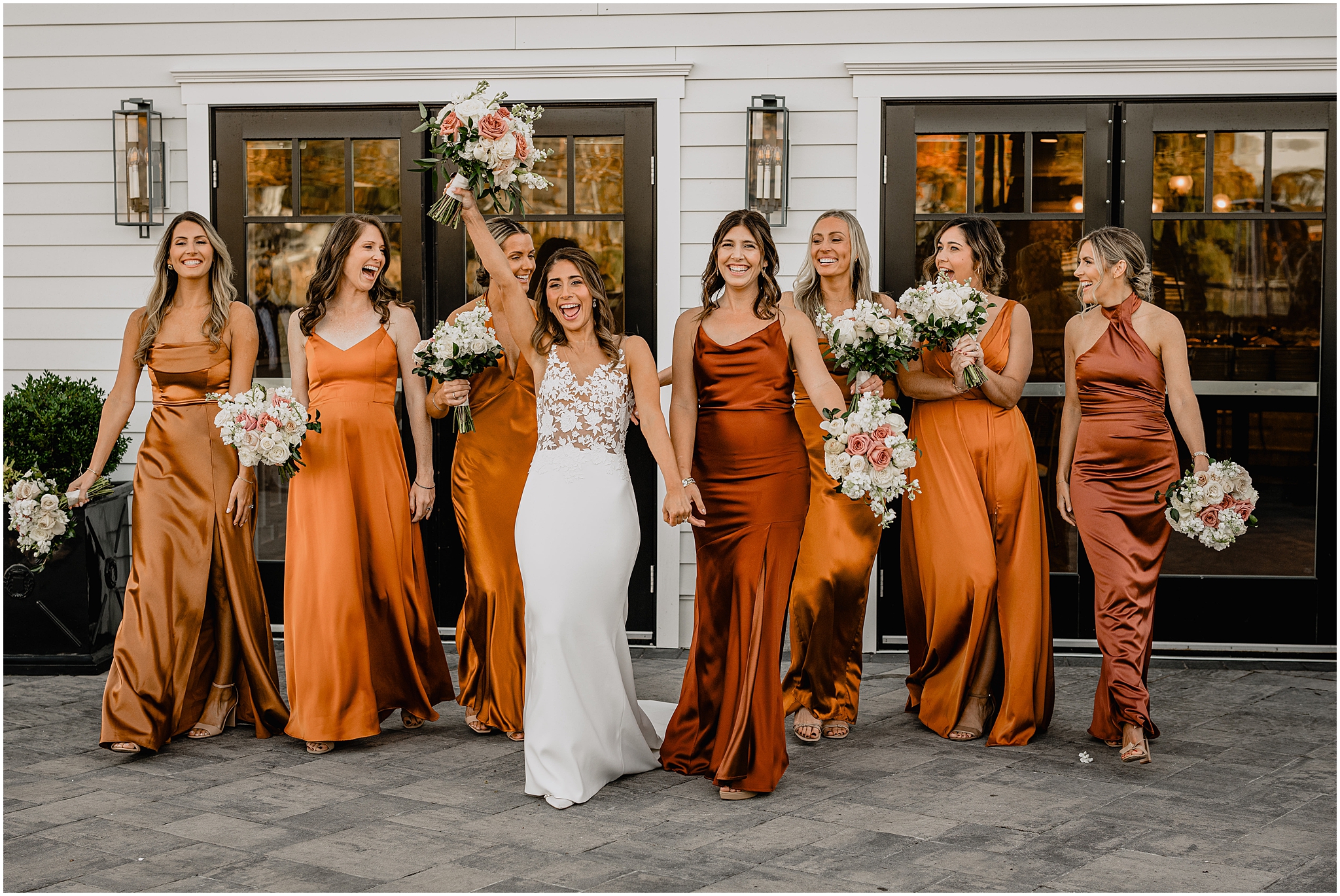 bride walks with bridesmaids in orange satin gowns outside the Waters Edge at Centerport