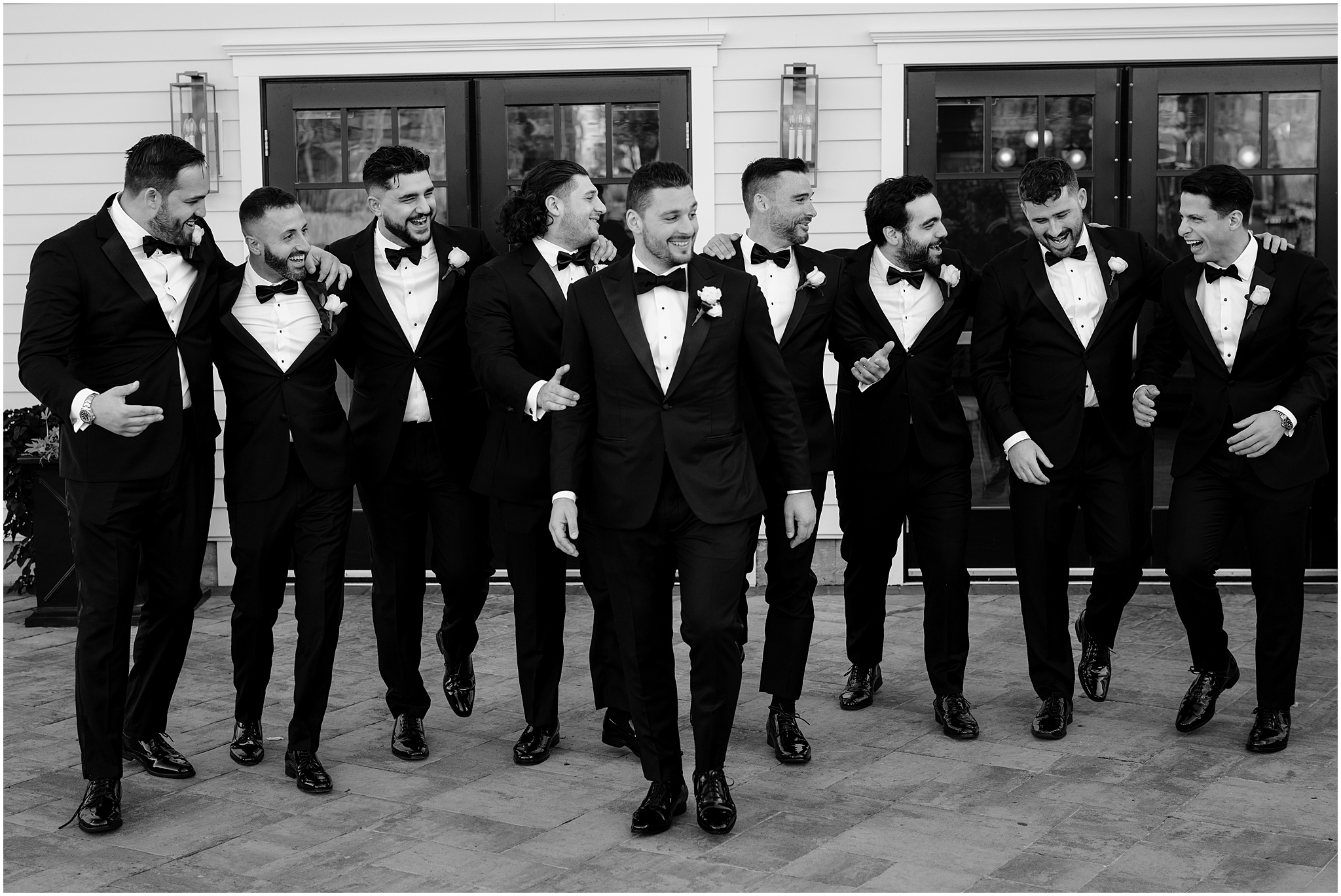 groom walks with groomsmen in black suit jackets on patio at the Waters Edge at Centerport