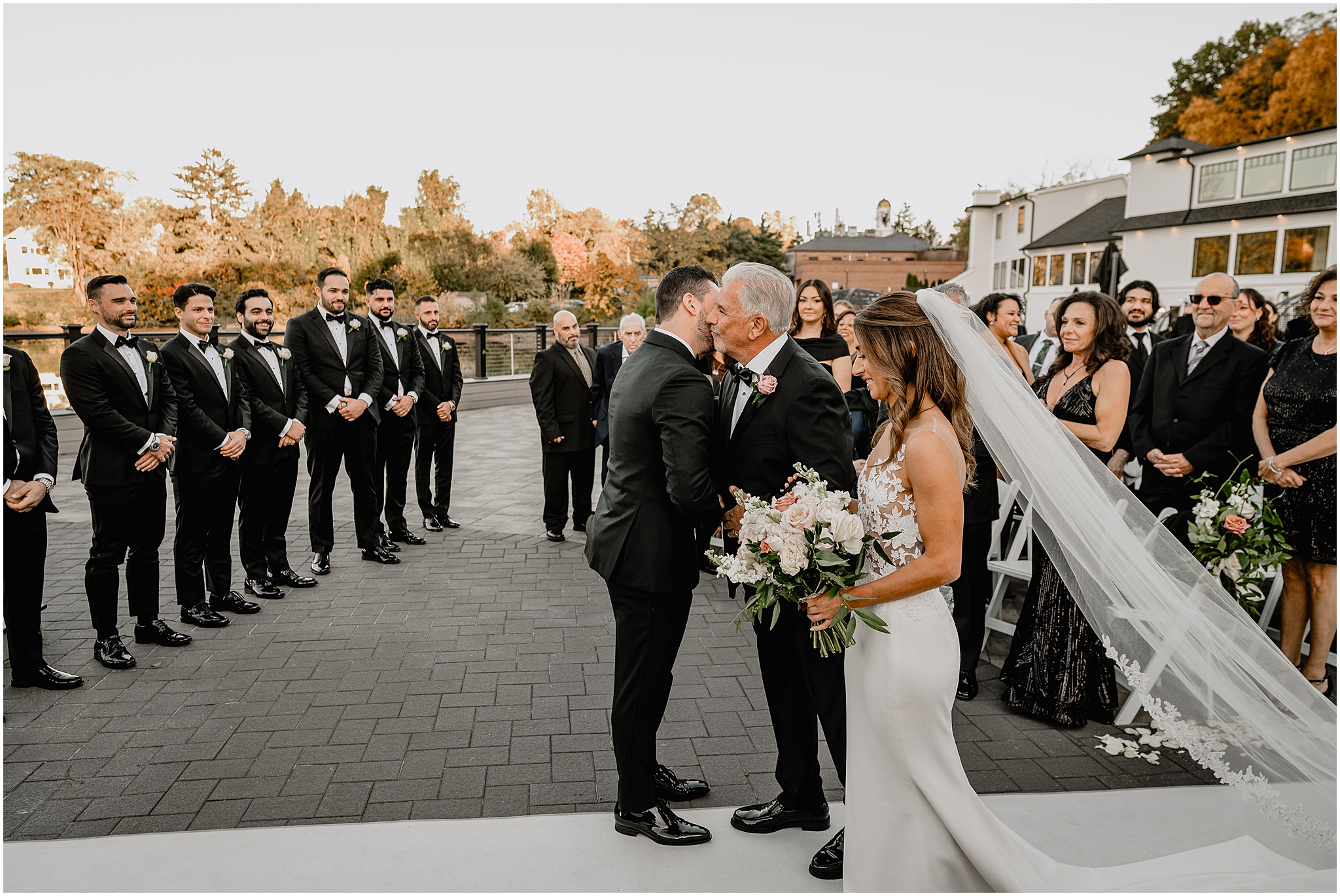 groom hugs bride's father during wedding ceremony on the patio at the Waters Edge at Centerport